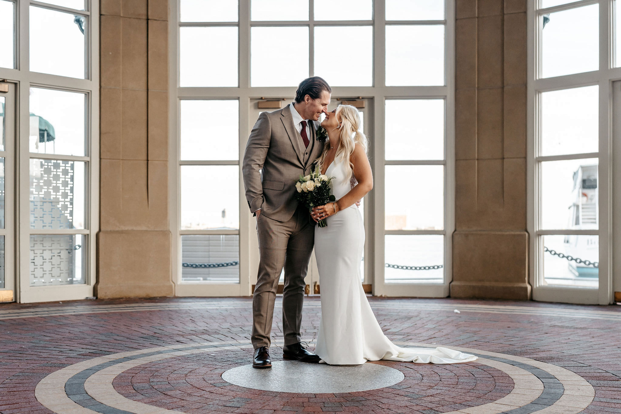 Bride and groom nose to nose in a sunlit rotunda with tall windows