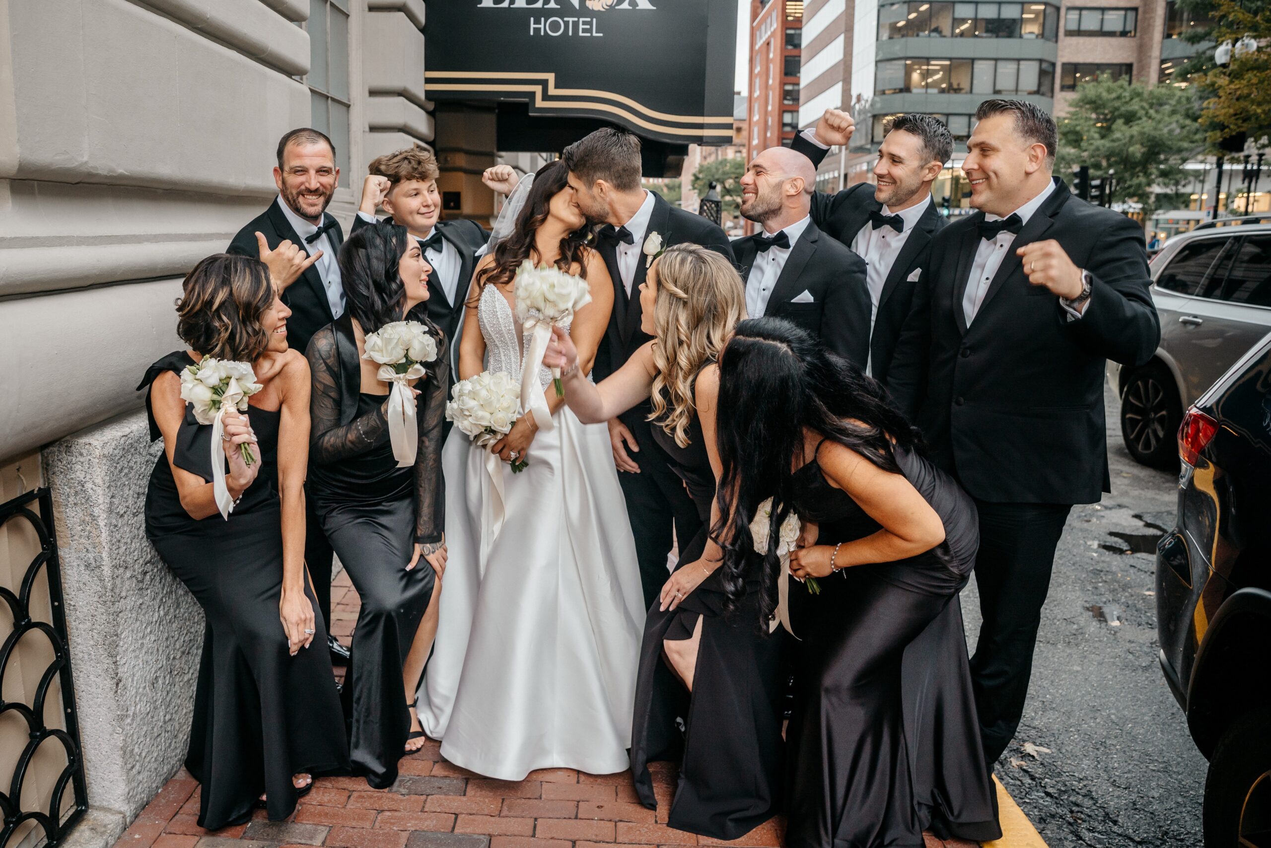 Bride and groom kissing with wedding party outside The Lenox Hotel Boston wedding venue, fun group photo in downtown Boston