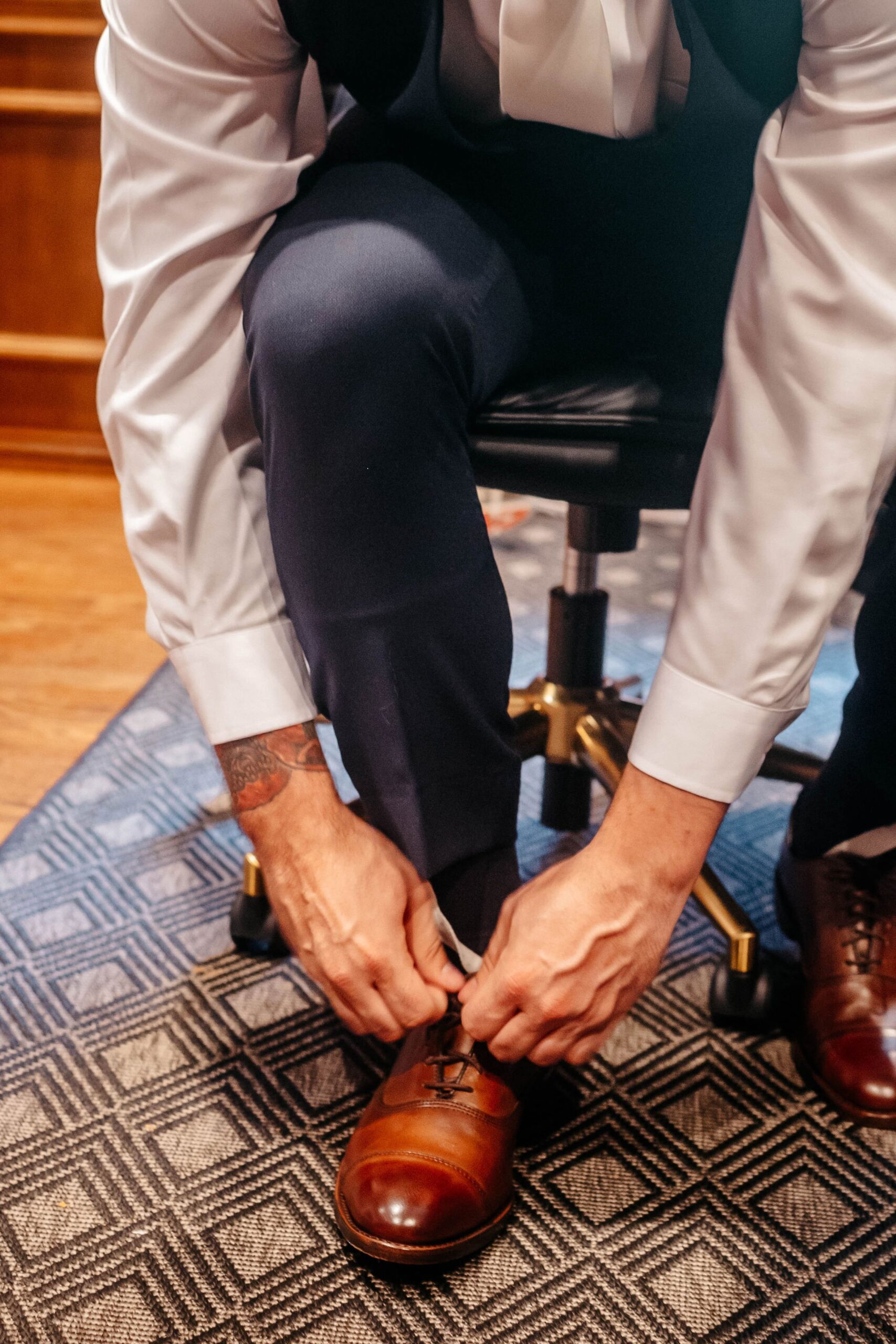 Groom tying brown dress shoes in hotel suite before ceremony at Boston hotel wedding venue
