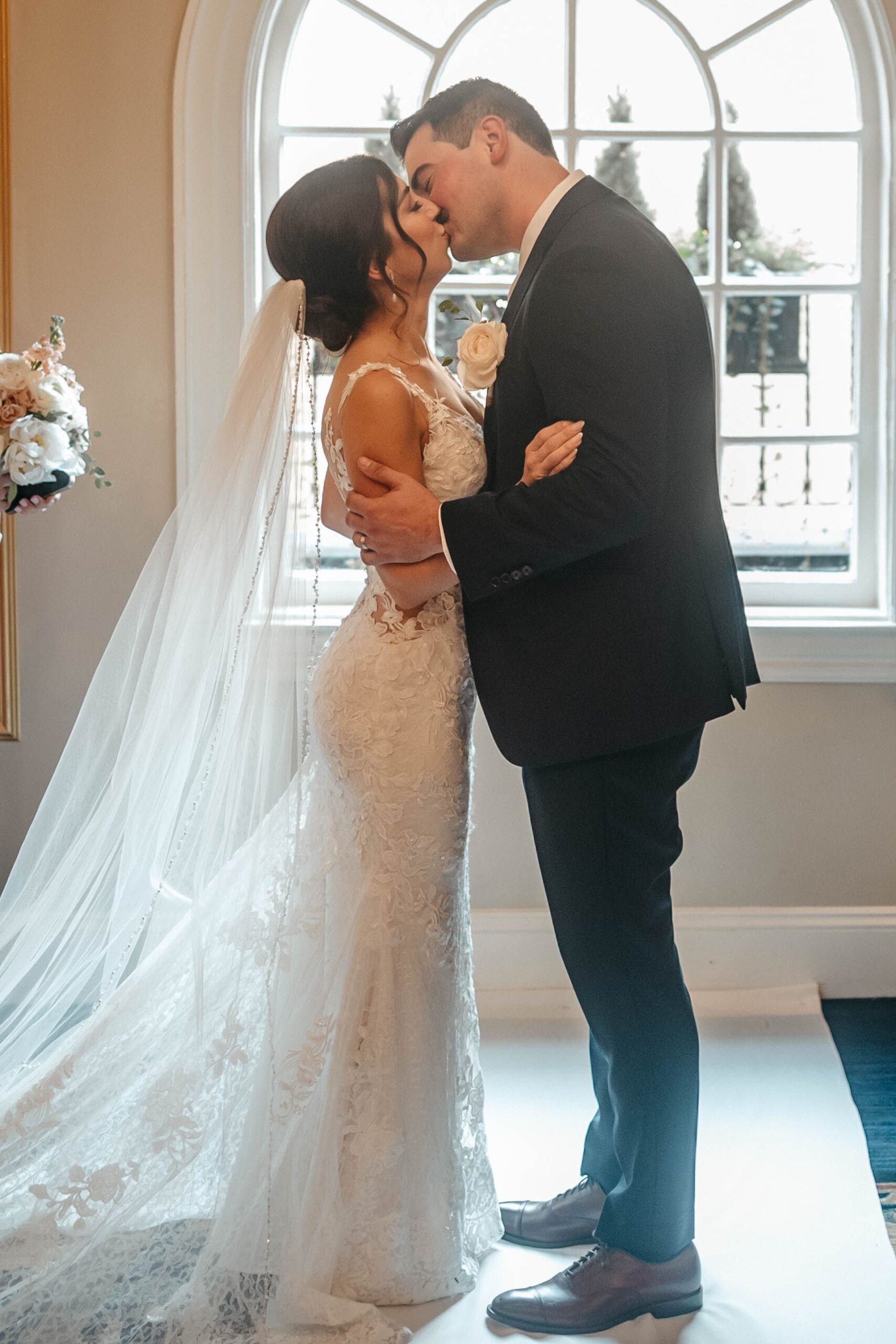 Bride and groom kissing by window with natural light at elegant Boston hotel wedding venue