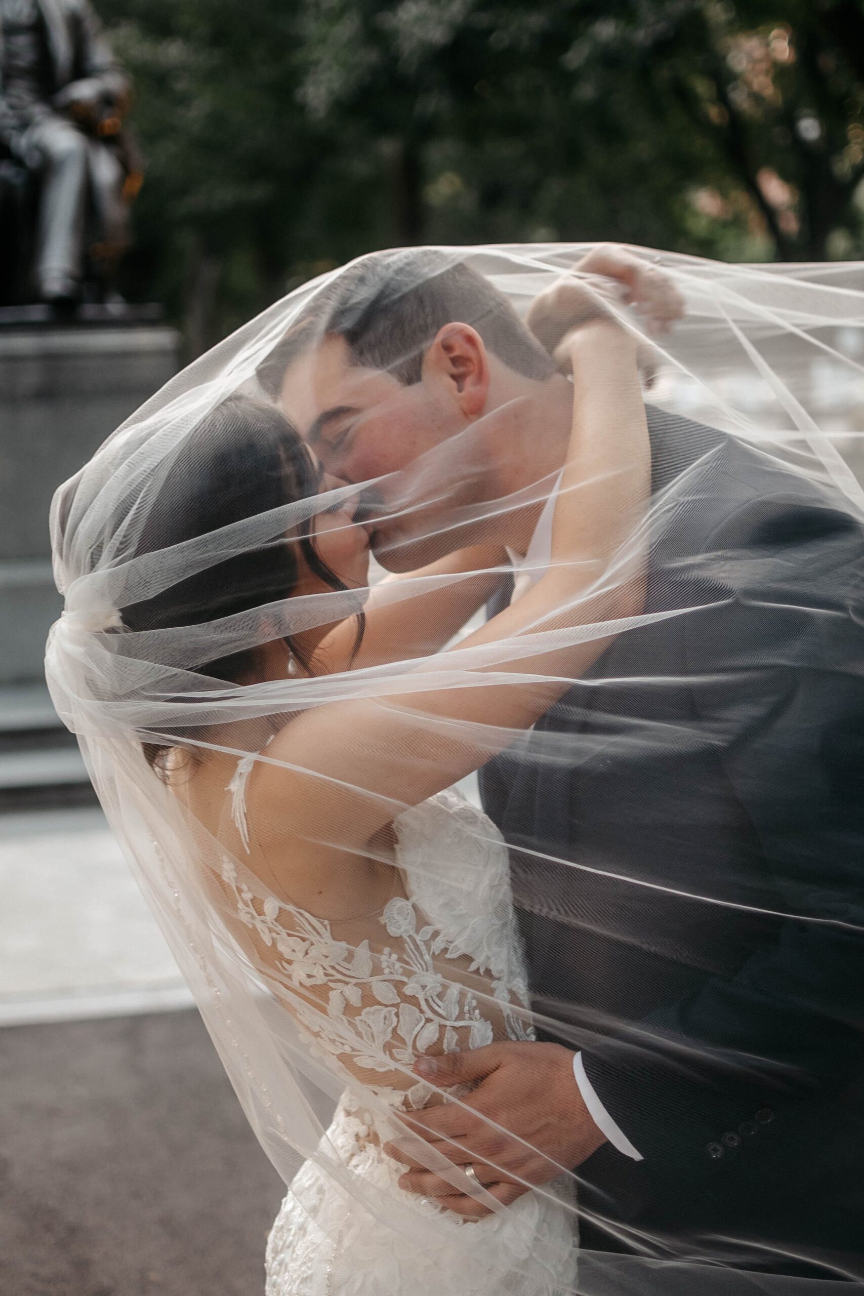 Bride and groom kissing under veil during Boston hotel wedding, intimate romantic moment outdoors