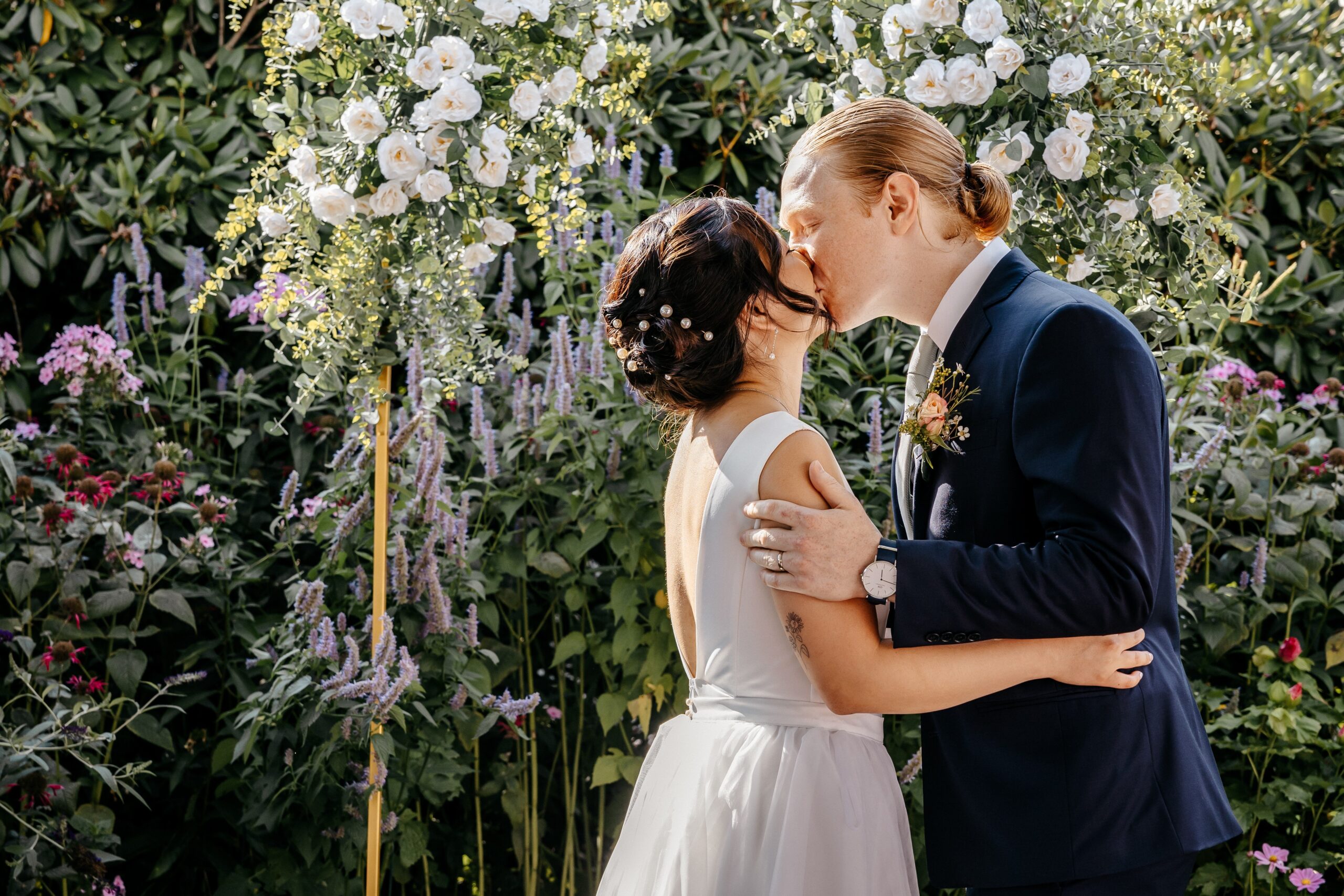 Couple kissing under floral arch during Boston wedding ceremony planned in a garden setting