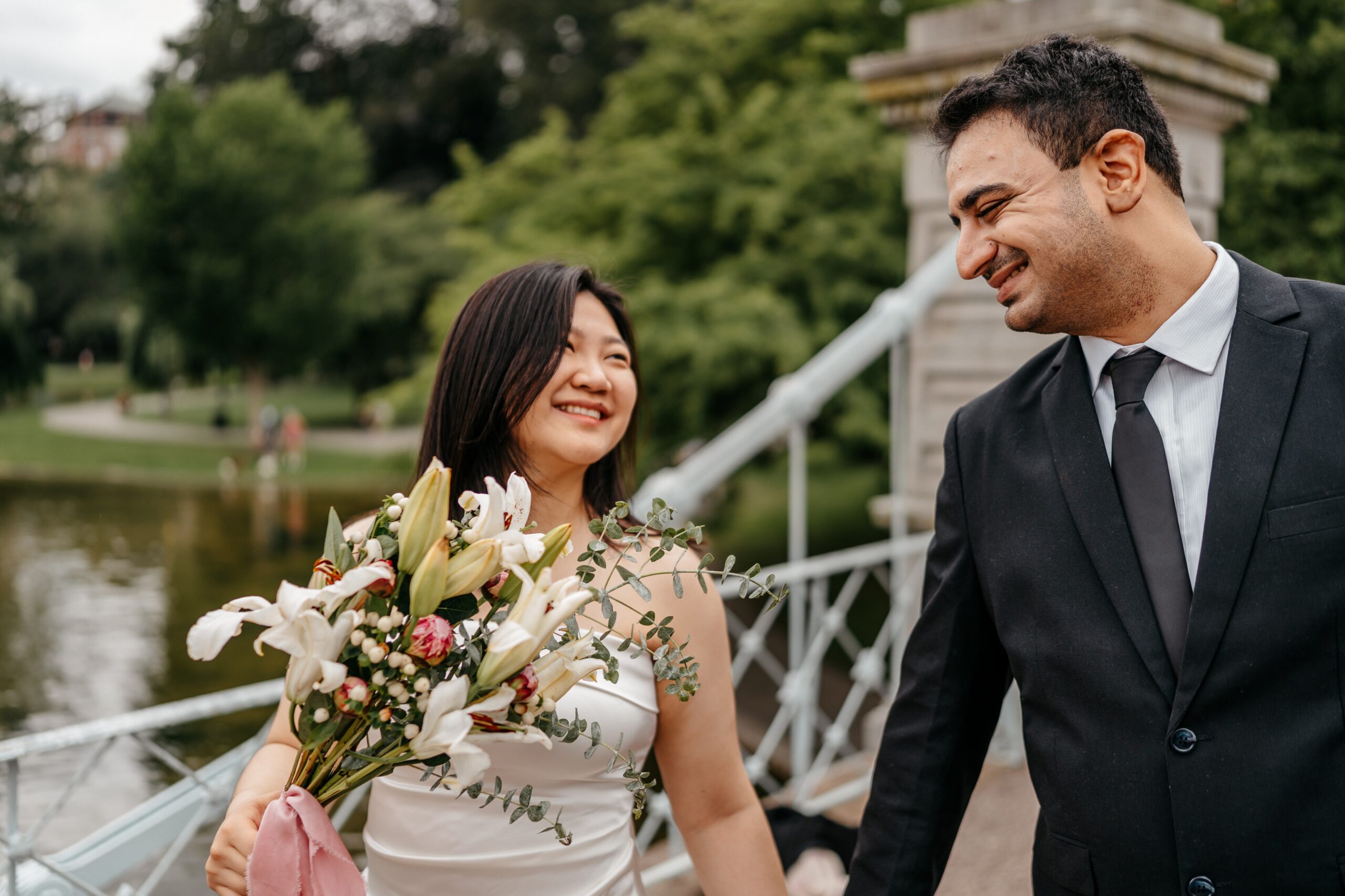Bride and groom walking together by waterfront with bouquet during Boston wedding planning portrait session