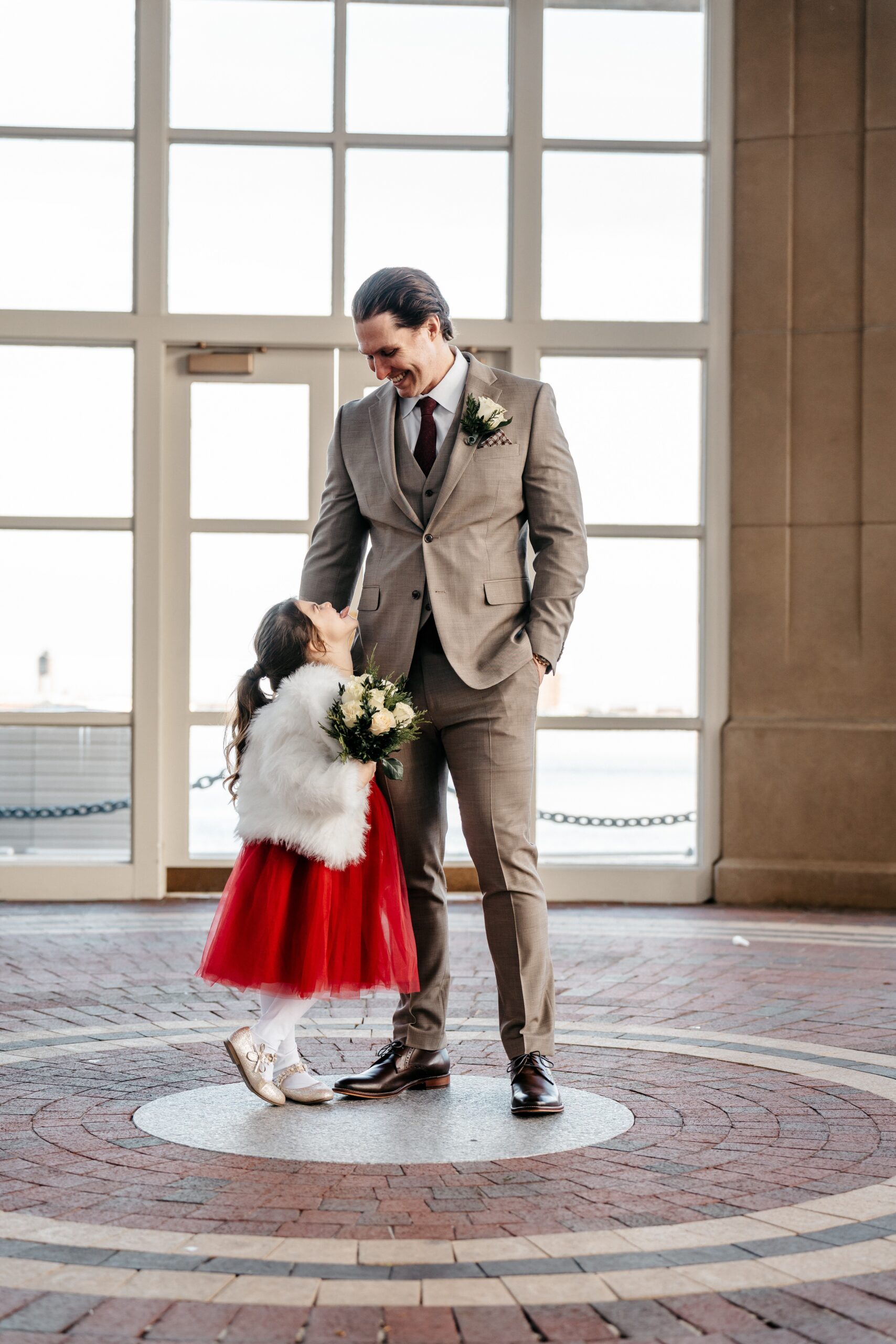 Groom with flower girl portrait in bright indoor space during Boston wedding