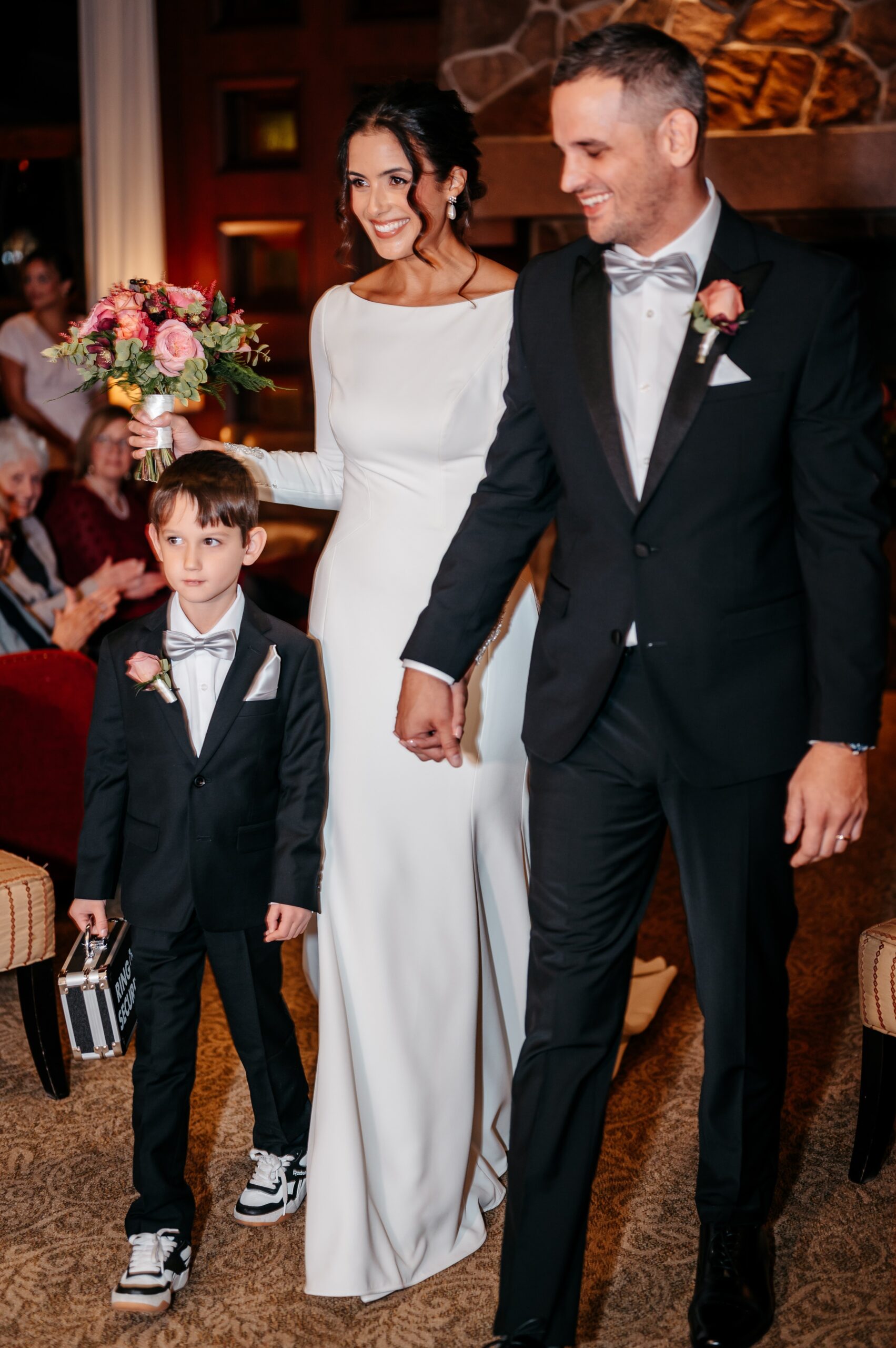 Newlyweds walking down aisle at Burlington wedding at Cafe Escadrille with child, joyful just-married celebration moment
