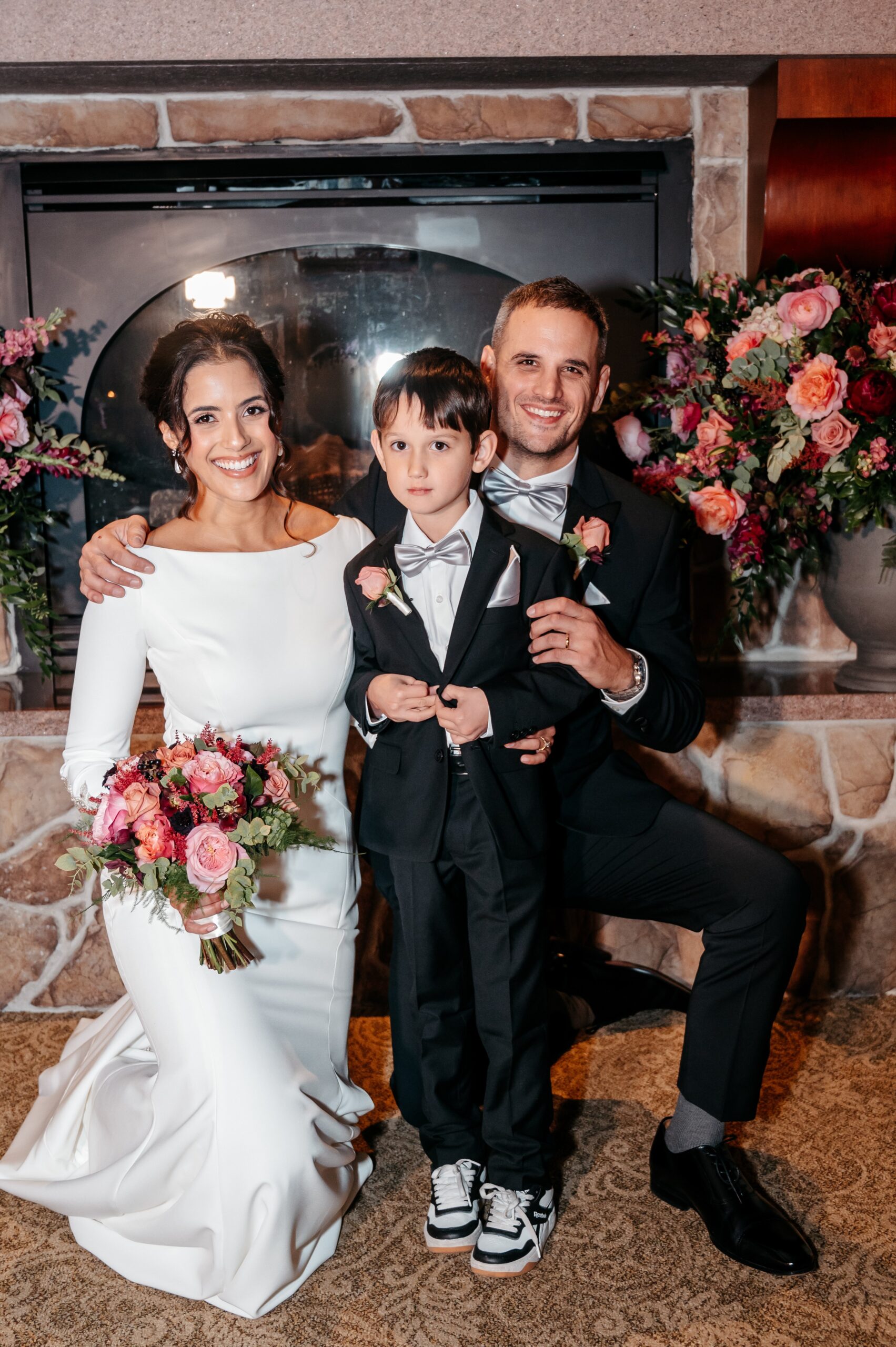 Bride and groom posing with child at Cafe Escadrille wedding in Burlington, joyful family portrait by fireplace