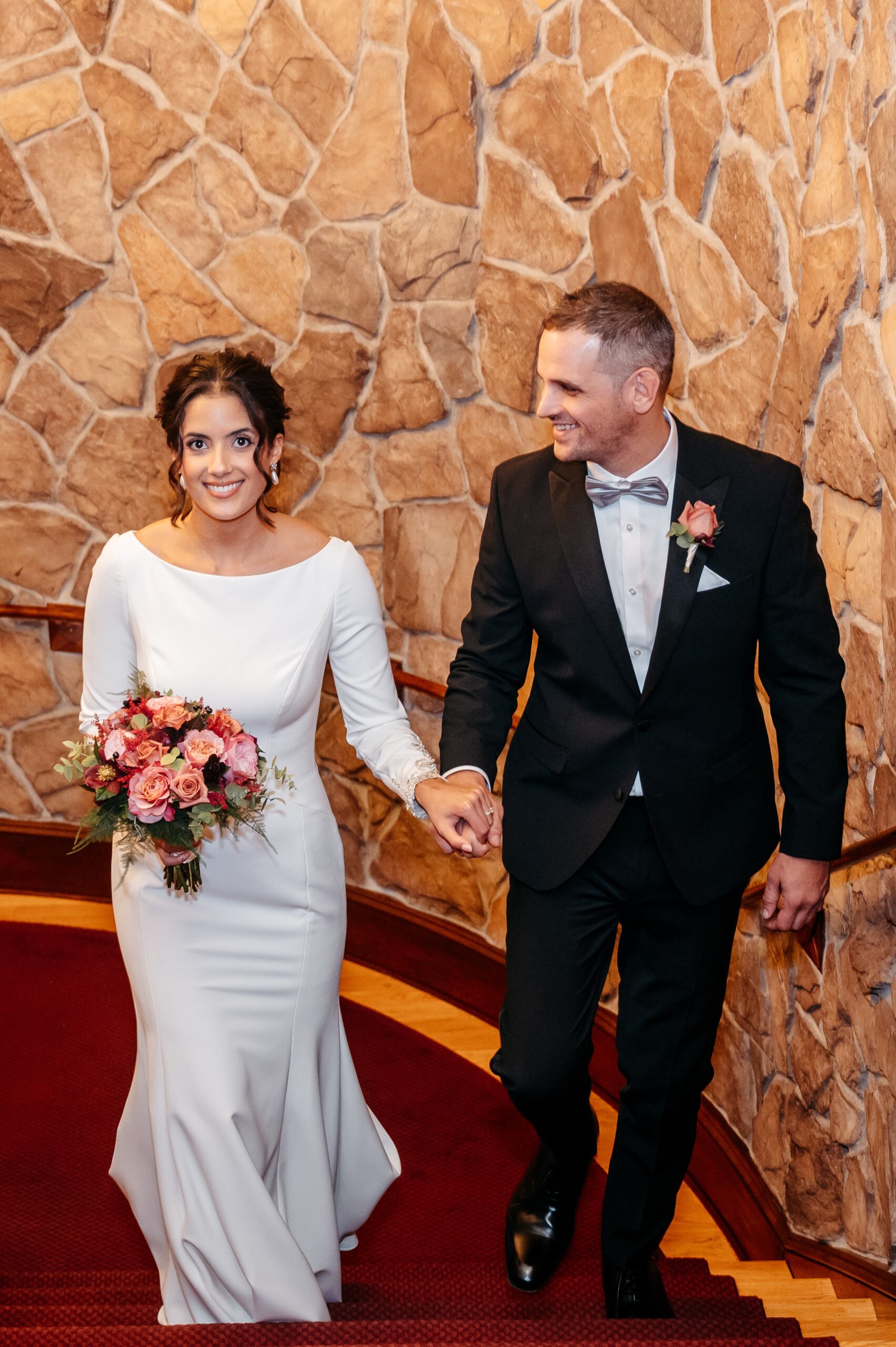 Bride and groom walking up staircase at Burlington wedding at Cafe Escadrille, romantic candid moment with stone wall backdrop