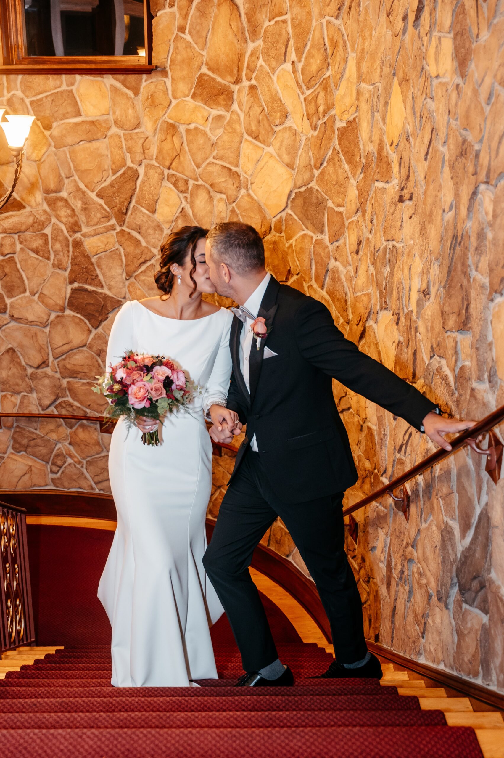 Couple sharing a kiss on staircase during Cafe Escadrille wedding in Burlington, intimate portrait with classic venue architecture