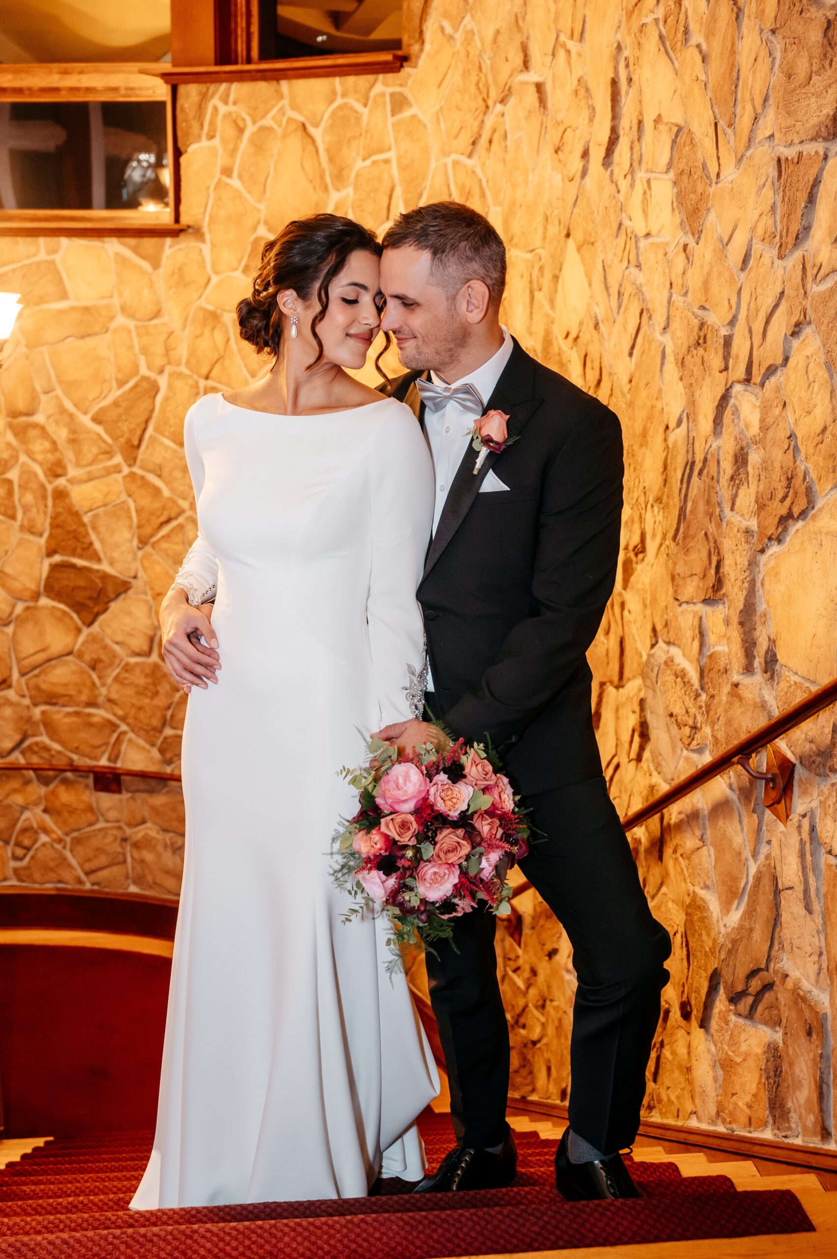 Bride and groom embracing on staircase at Burlington wedding at Cafe Escadrille, soft romantic portrait with floral bouquet