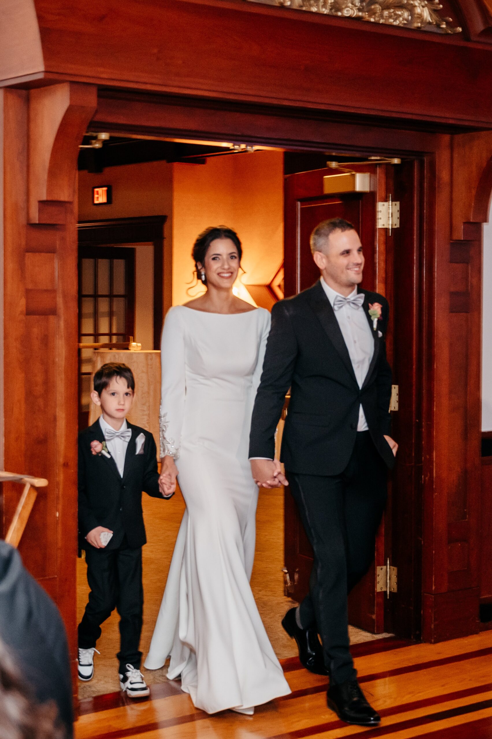 Bride and groom entering reception with child at Burlington wedding at Cafe Escadrille, joyful moment reflecting full wedding experience and cost considerations