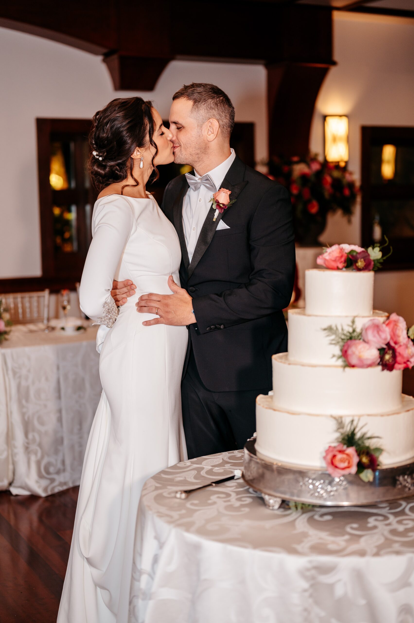 Bride and groom kissing beside wedding cake at Cafe Escadrille Burlington reception, romantic moment highlighting venue details