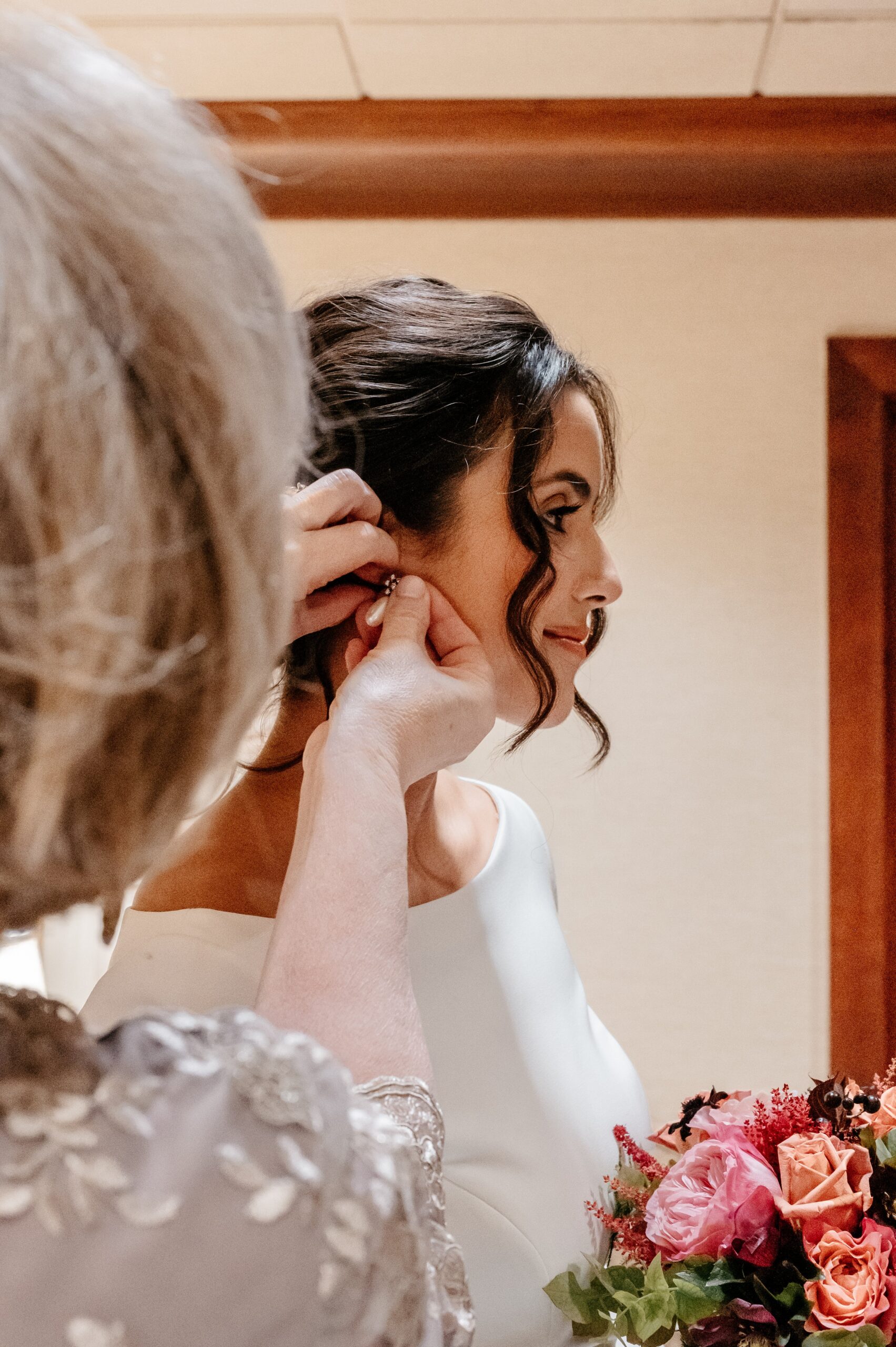 Bride having earrings fastened while holding bouquet before Cafe Escadrille wedding in Burlington, soft emotional getting-ready detail