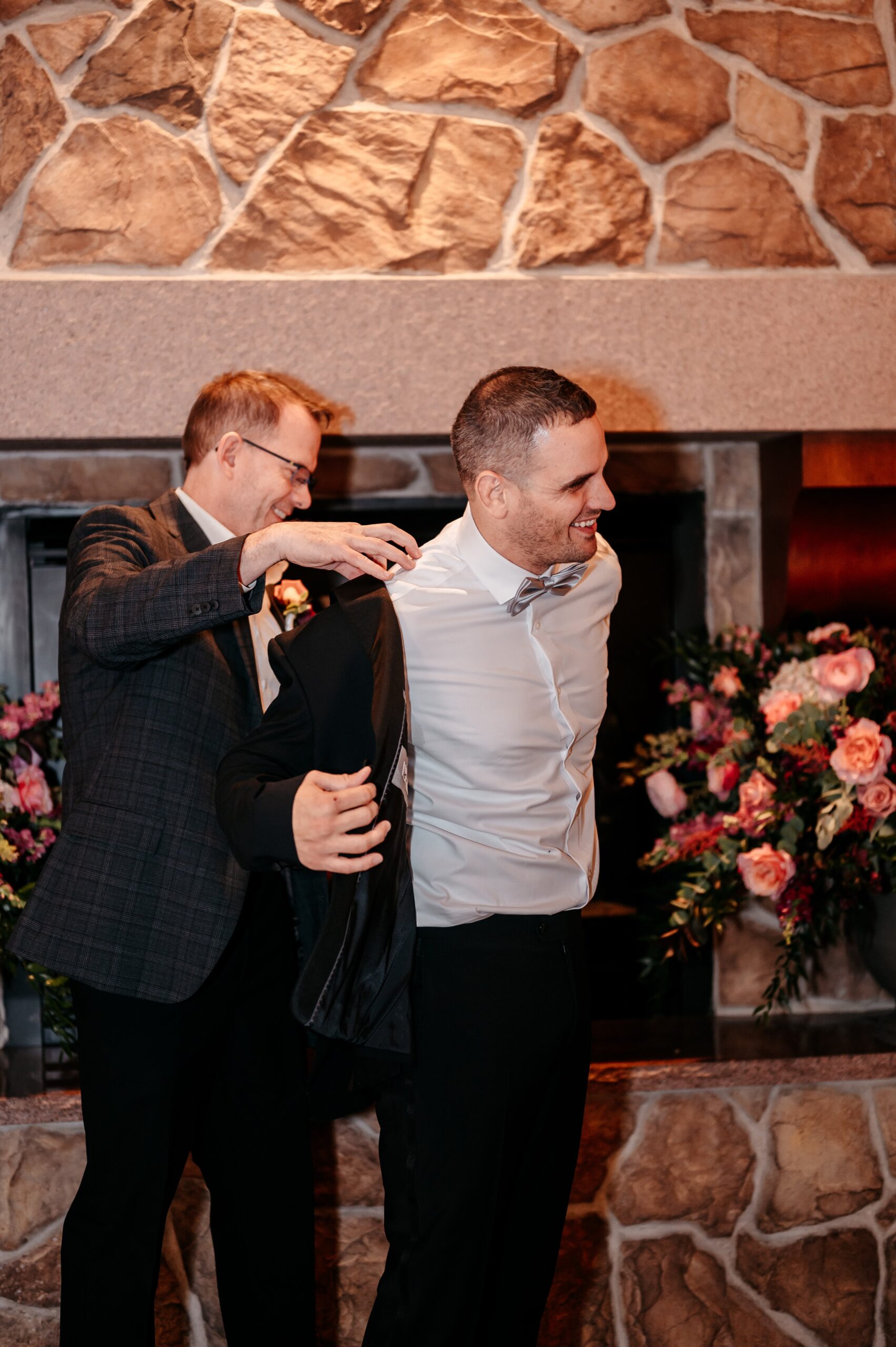 Groom getting ready with help putting on jacket during Cafe Escadrille wedding in Burlington, candid pre-ceremony moment