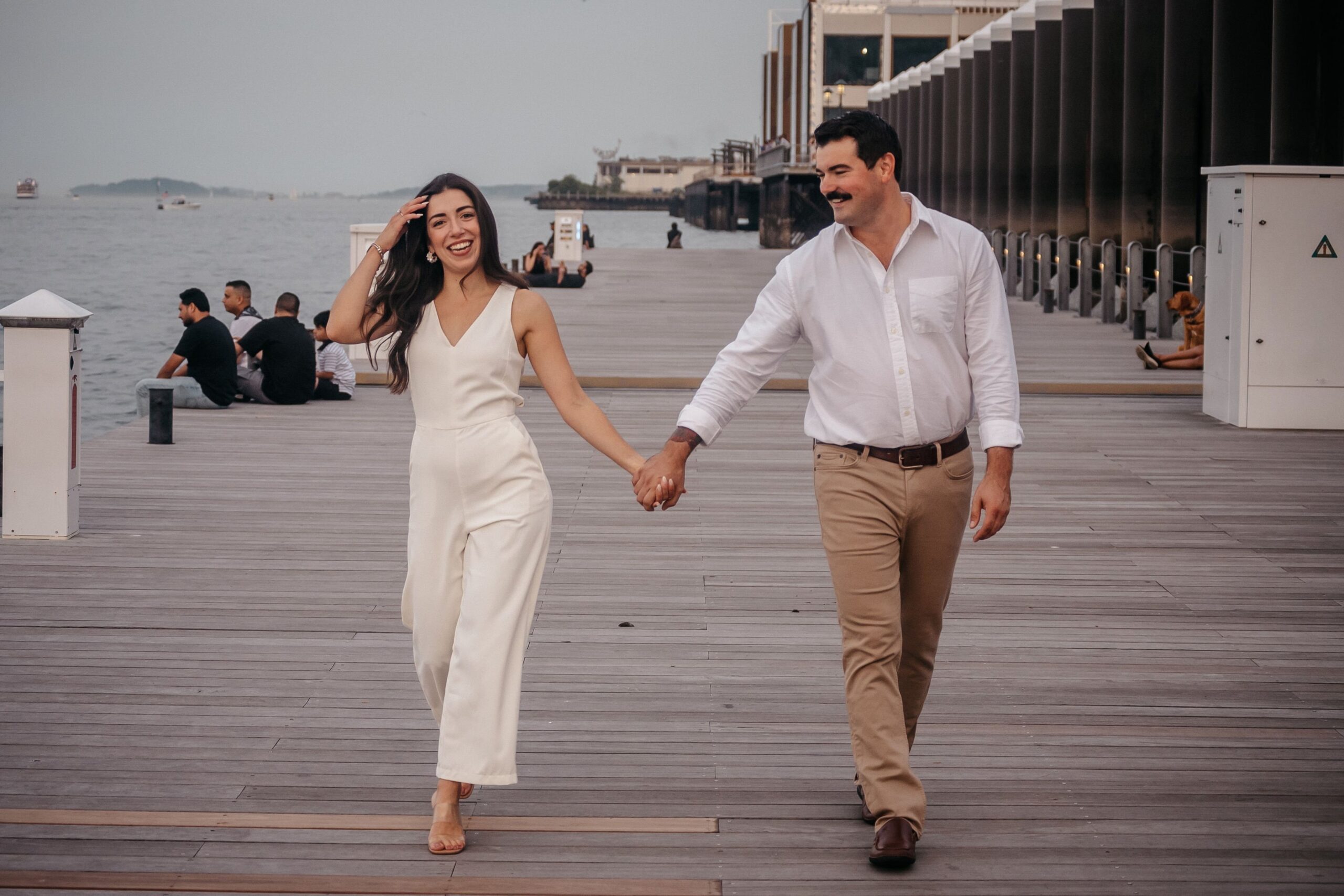 Couple walking hand in hand during Fan Pier Park engagement session in Boston, relaxed waterfront moment on the pier