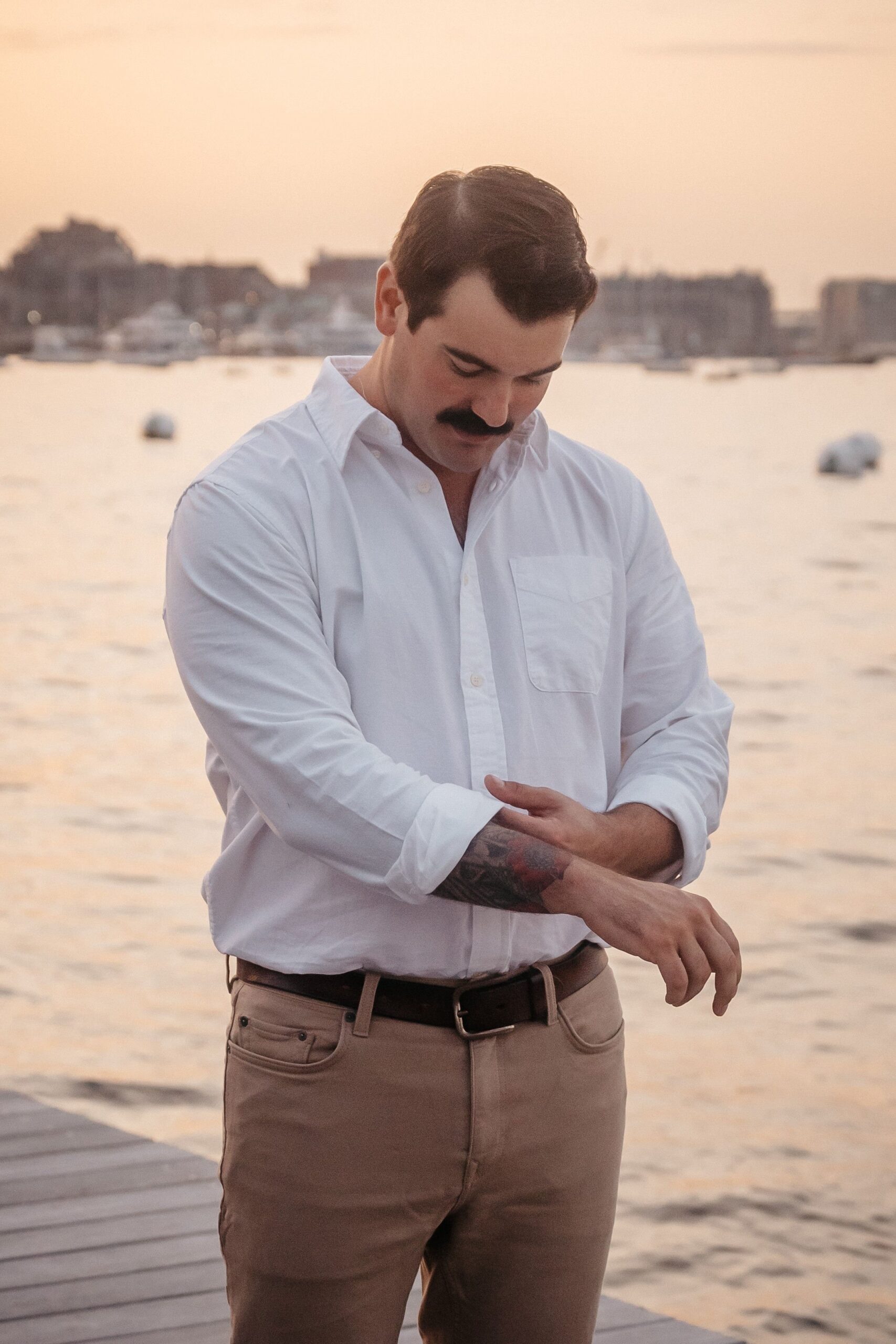 Groom getting ready during Fan Pier Park engagement session, candid detail portrait on Boston waterfront at sunset