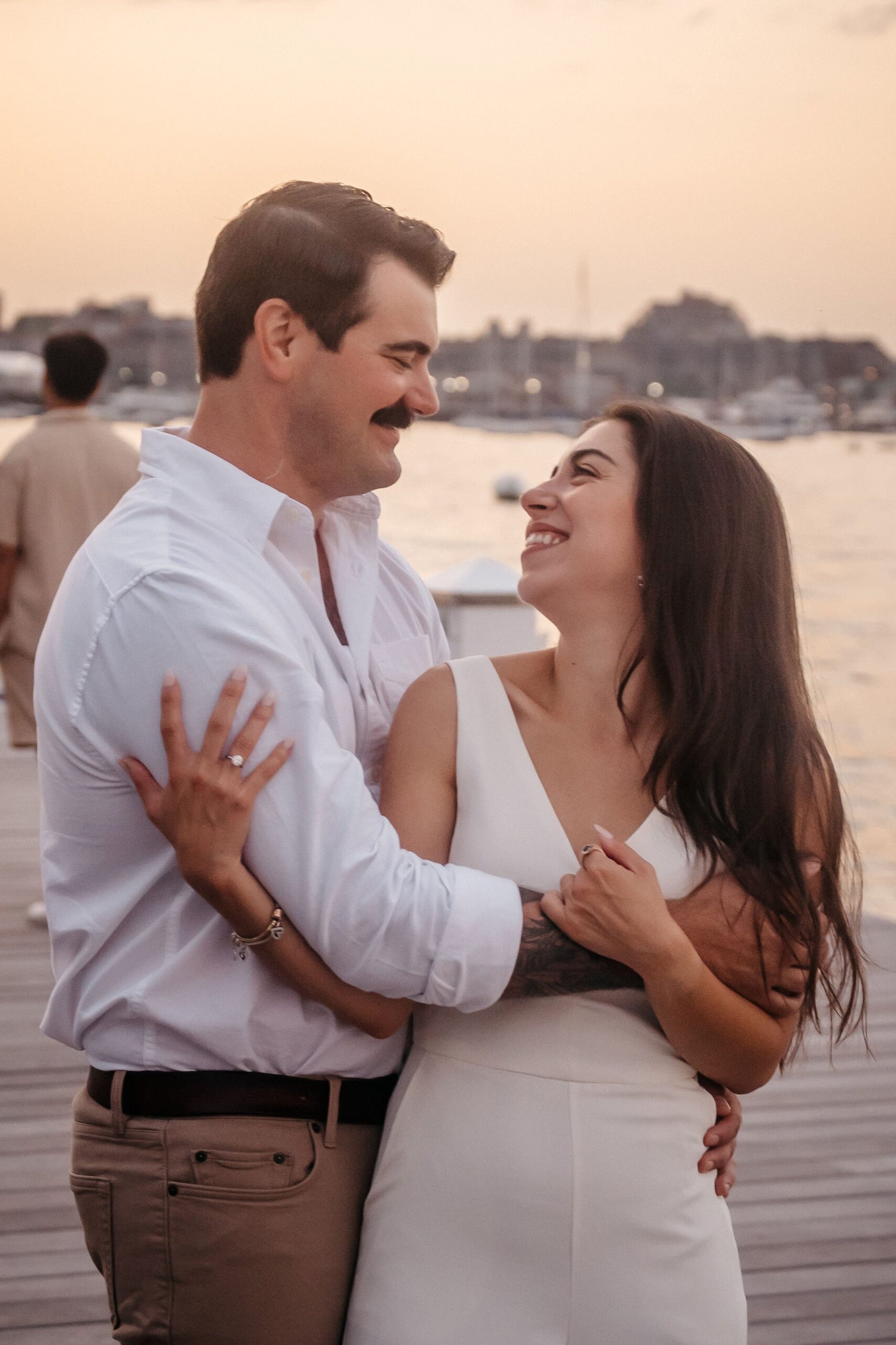 Romantic couple smiling at each other during Fan Pier Park engagement session, golden sunset light on the Boston waterfront