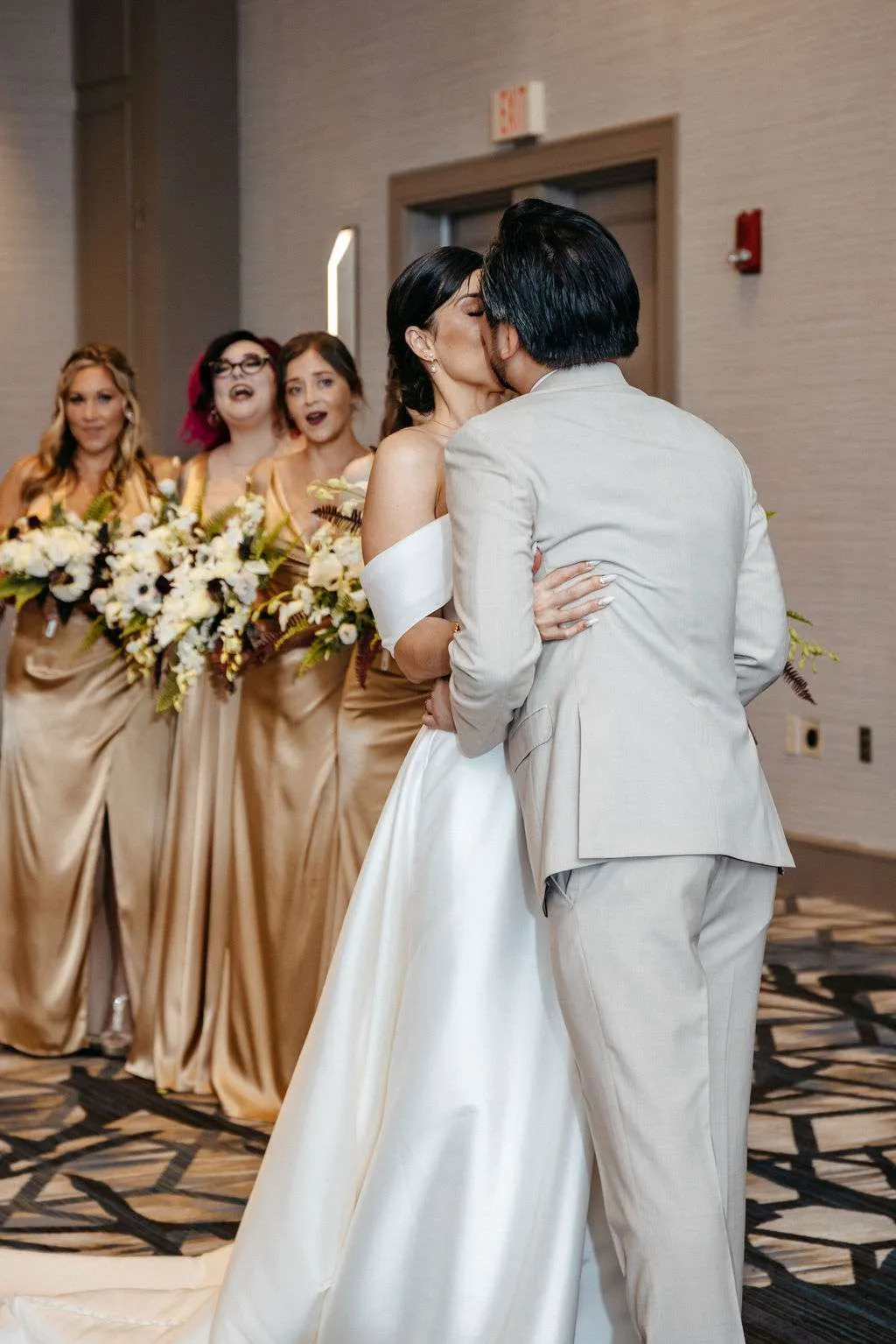 Husband kisses wife at their wedding ceremony and bridesmaids cheer in the background at their Burlington wedding locations 
