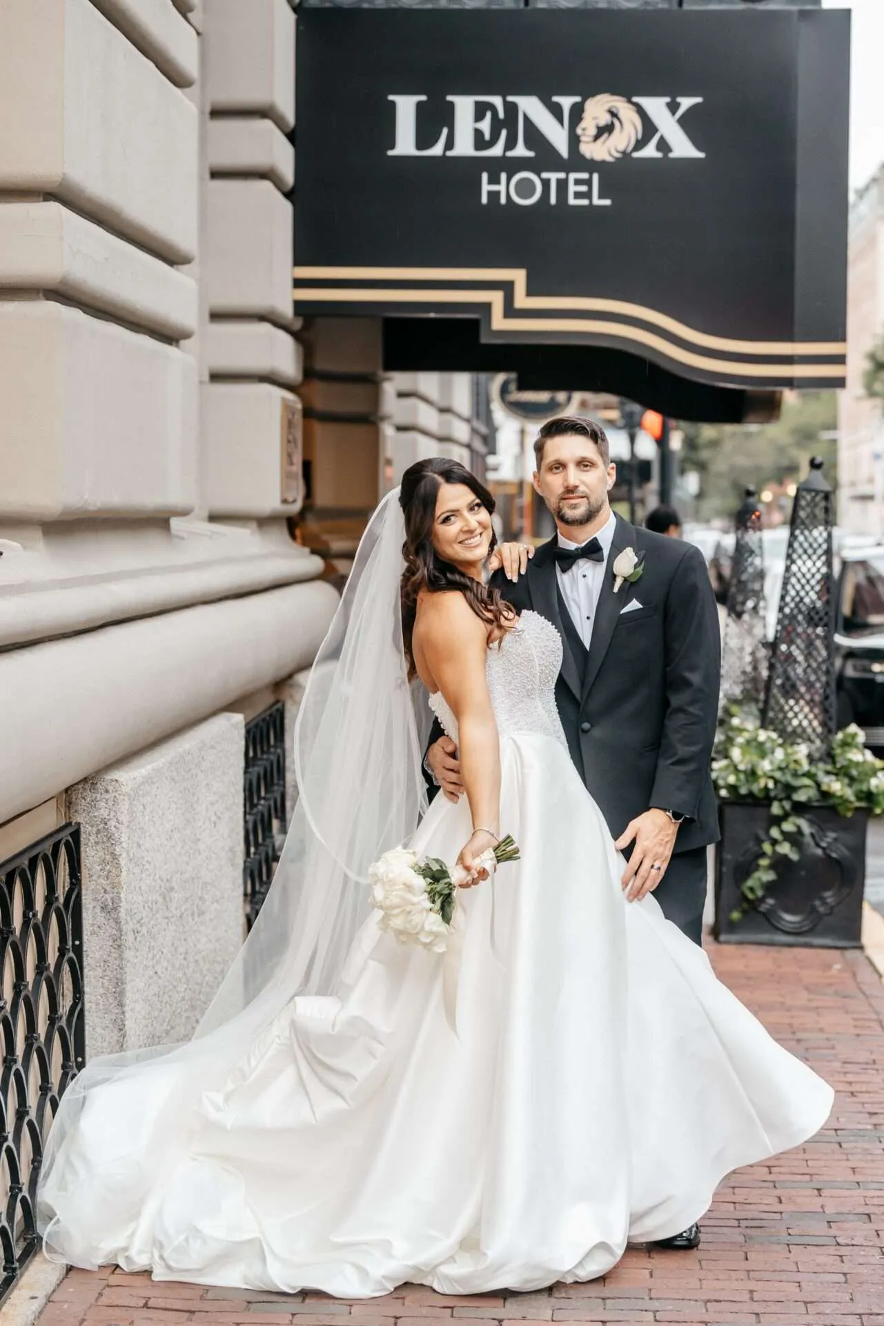Bride and groom pose with bouquet in front of the Lenox Hotel while getting married in massachusetts