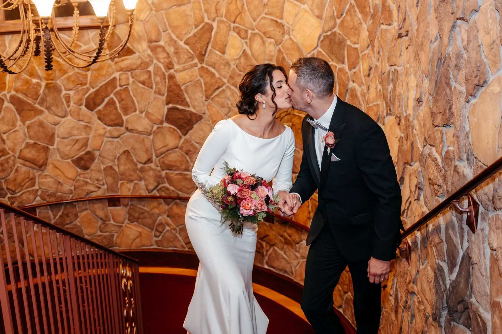 Bride an groom share a kiss as they climb a staircase while getting married in massachusetts