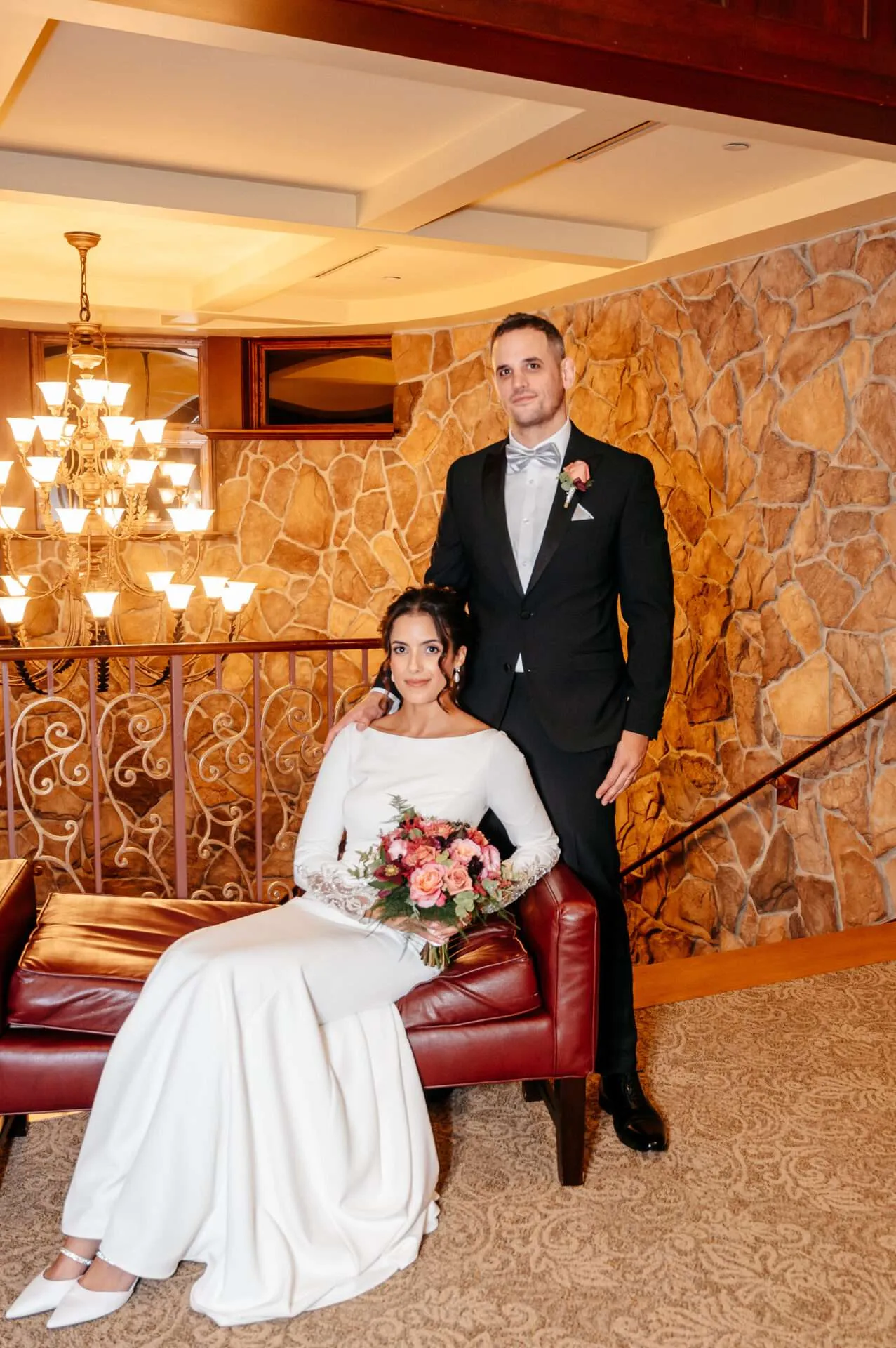 Husband and wife pose and smile in front of a chandelier while getting married in massachusetts