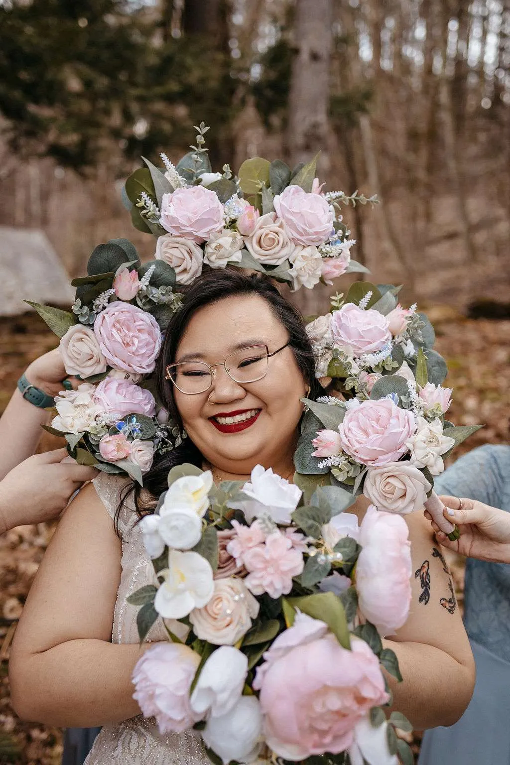 Bride with glasses and red lipstick is surrounded by pink flower bouquets knowing the average cost of Boston wedding