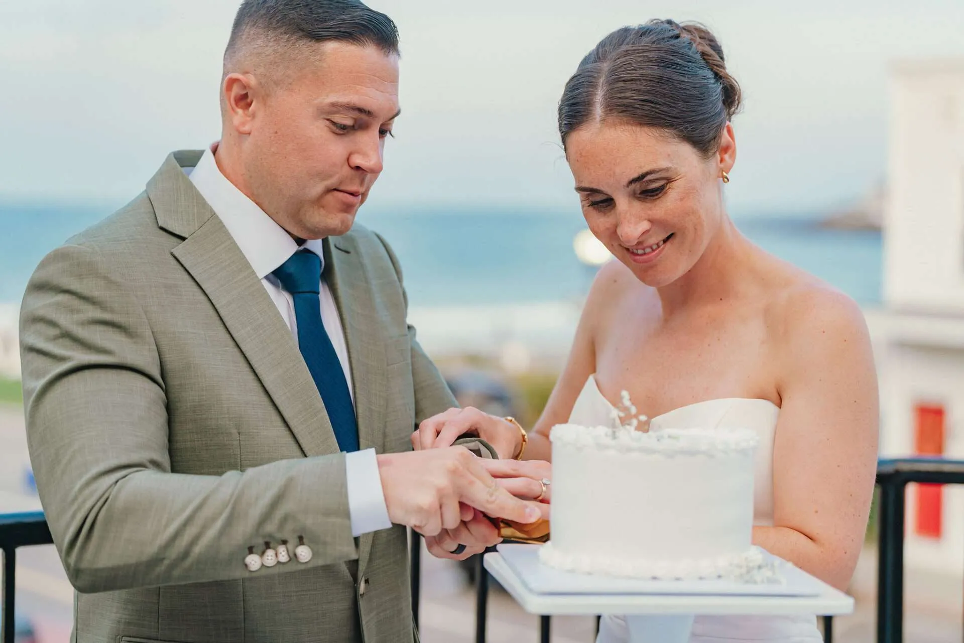 A bride and groom cut their small white wedding cake at their seaport wedding venue with harbor views