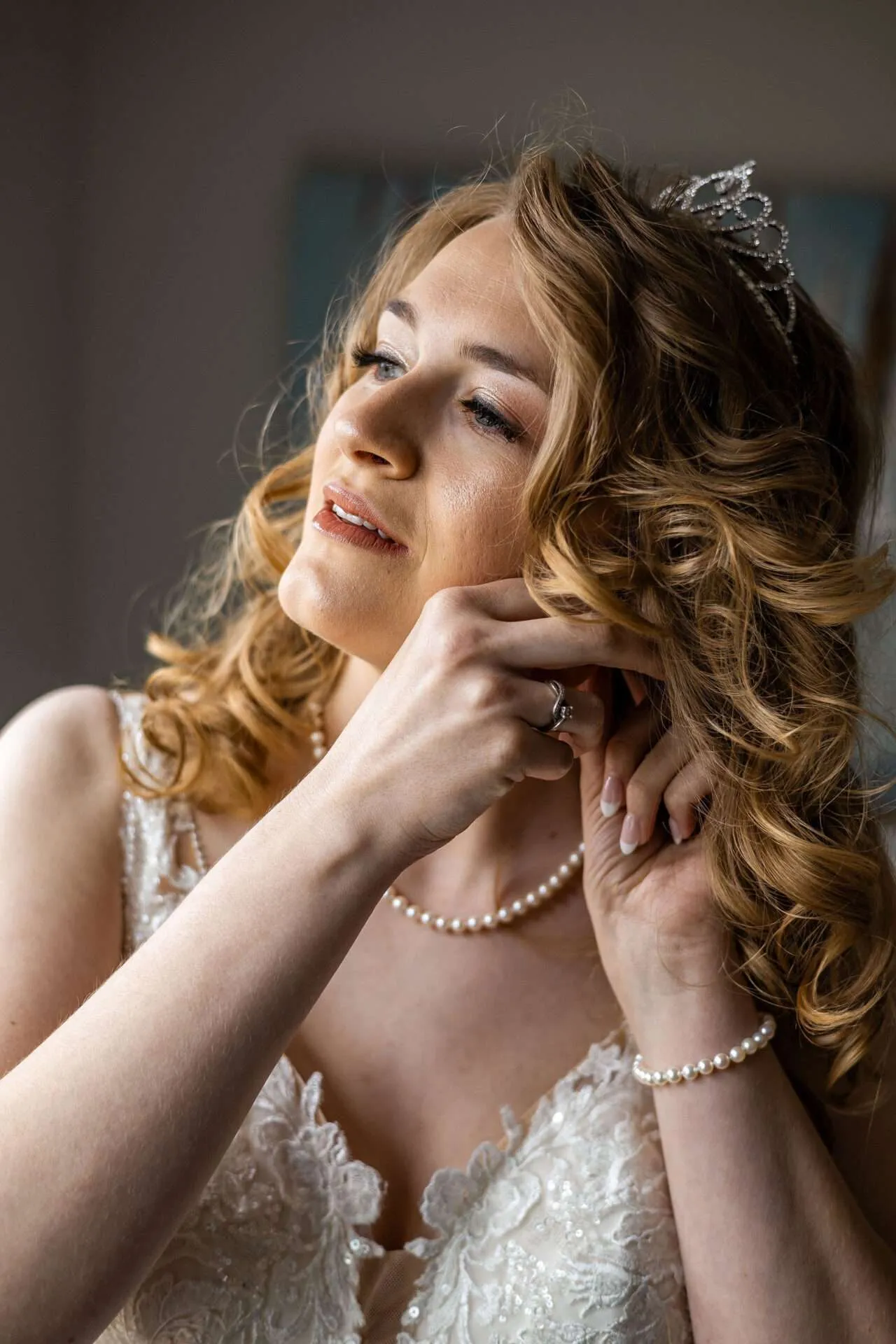 A bride wearing a tiara and pearls puts her earring on to get ready for her wedding at a Seaport Boston wedding venue