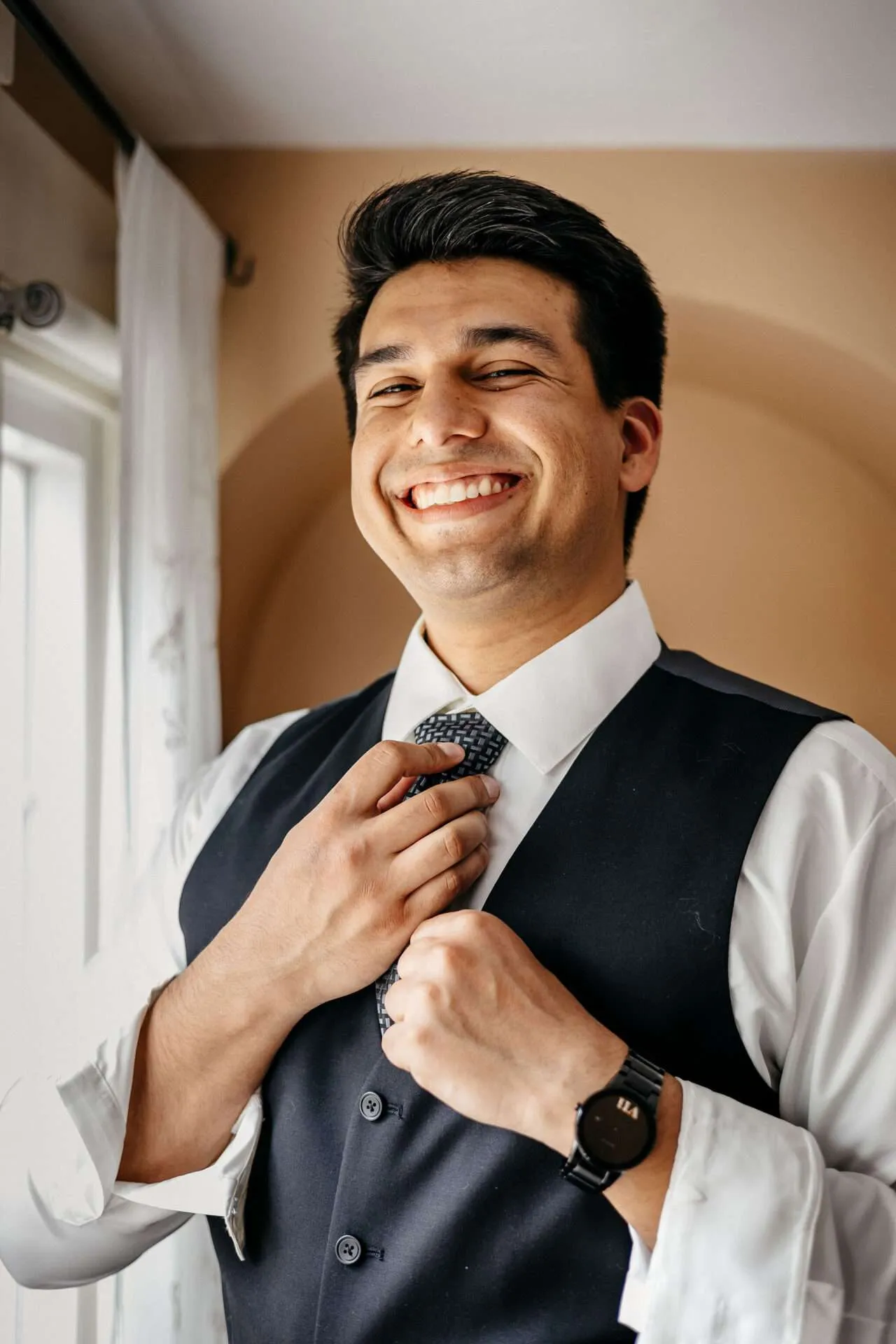 A groom smiles and adjusts his tie while getting ready for his wedding at a Boston Seaport wedding venue