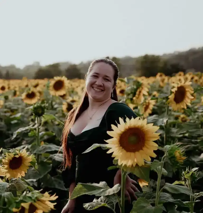 Nina Borseth of Love in Focus Studio, a team of New England photographers, standing in a sunflower field