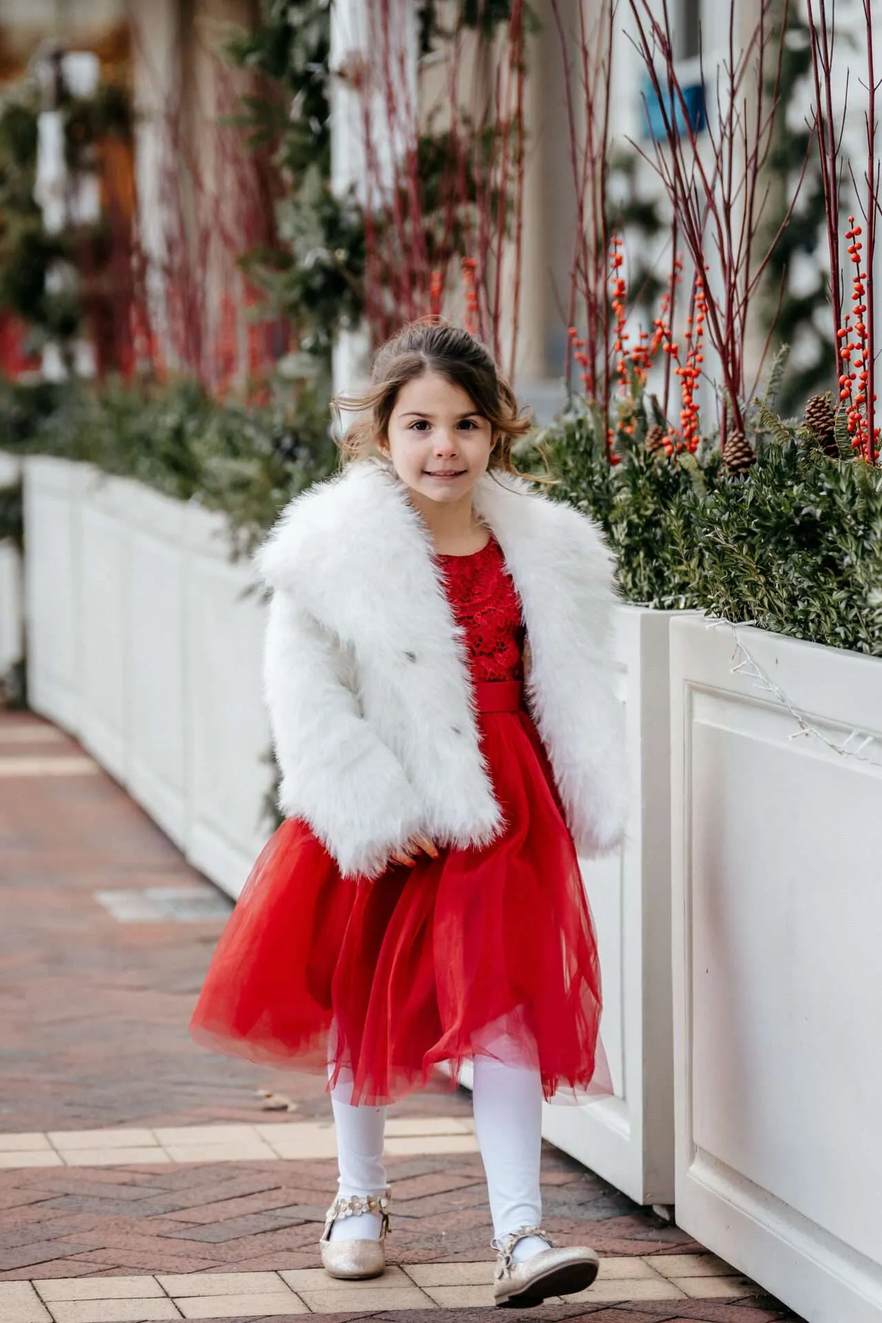 A little girl in a red dress and white fur coat walk towards her parents while a Boston city hall elopement photographer takes pictures 