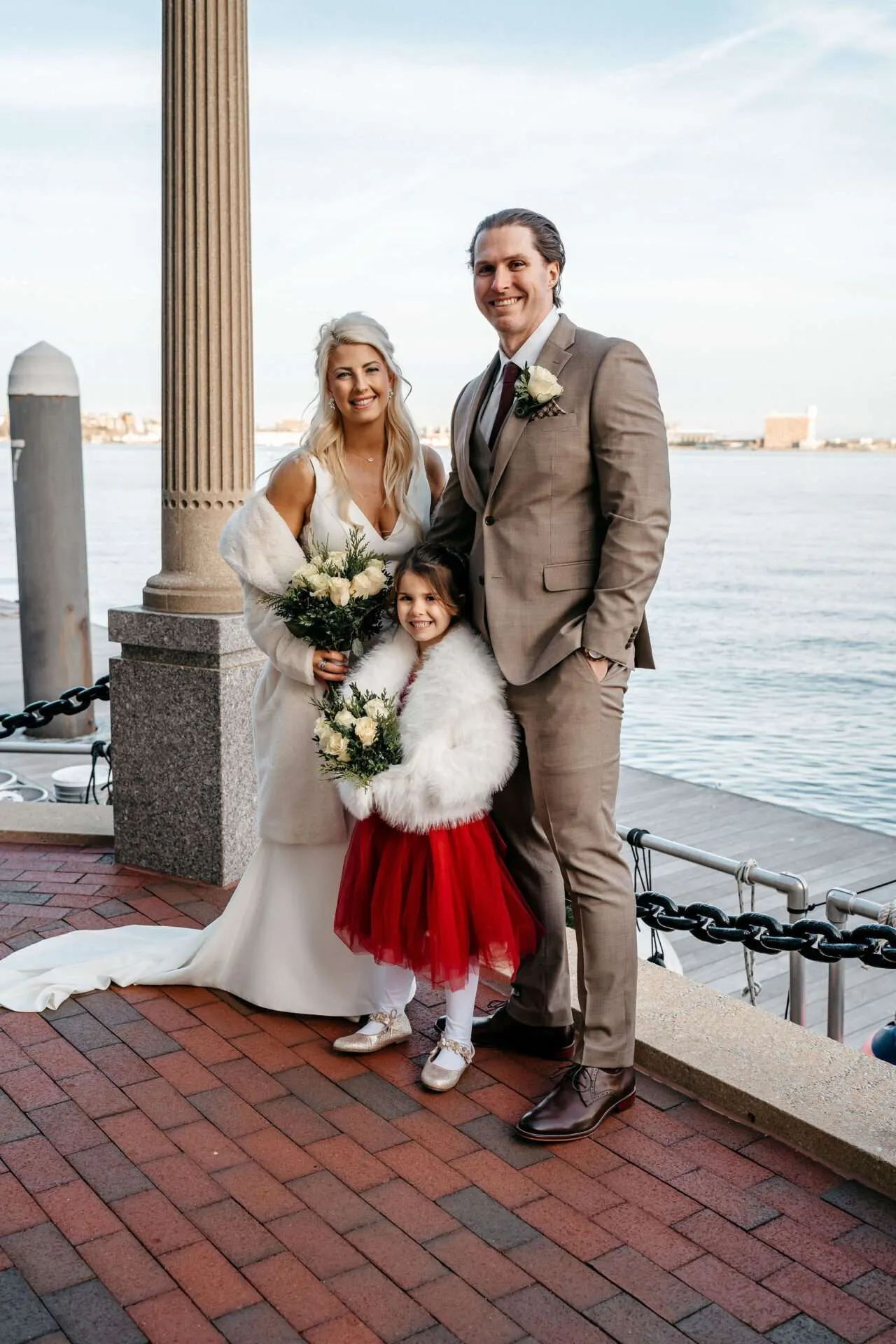 Bride and groom smile and stand in front of the Boston harbor with one of the best wedding photographers in boston