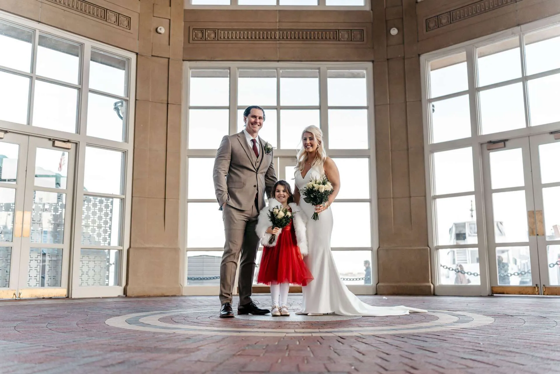 A bride and groom stand with their dauther and pose for Boston city hall wedding photos