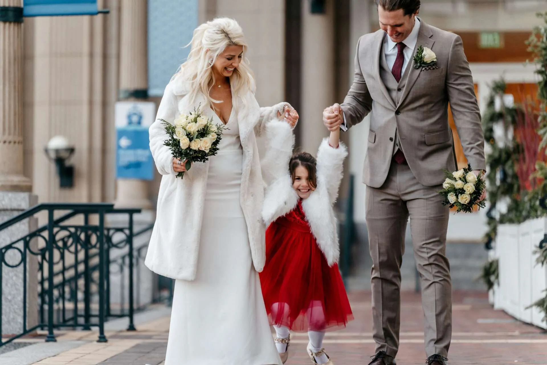 Bride and groom hold their daughter's hands while walking down the sidewalk after getting married at city hall Boston