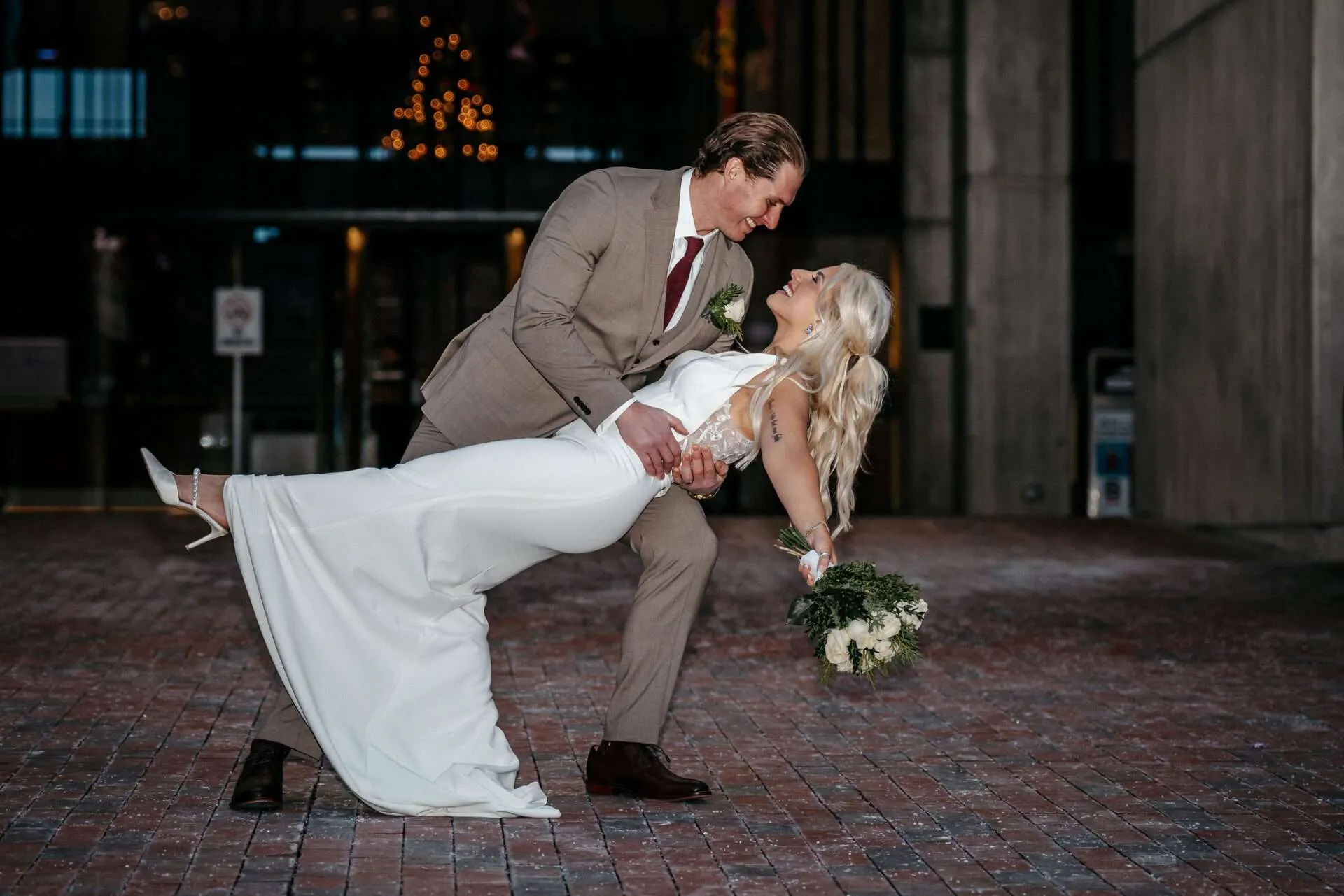 Groom dipping his bride on the brick plaza outside Boston City Hall at dusk