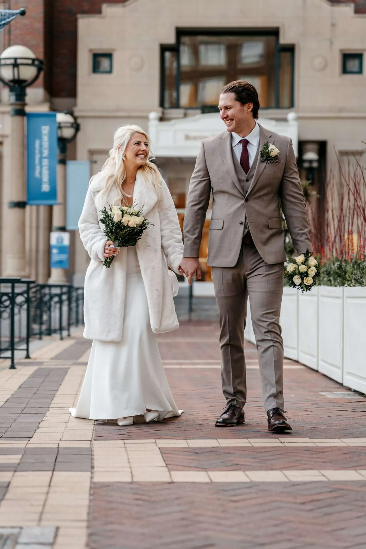 Bride and groom walk down the sidewalk during Christmas time talking about how to get married at Boston city hall
