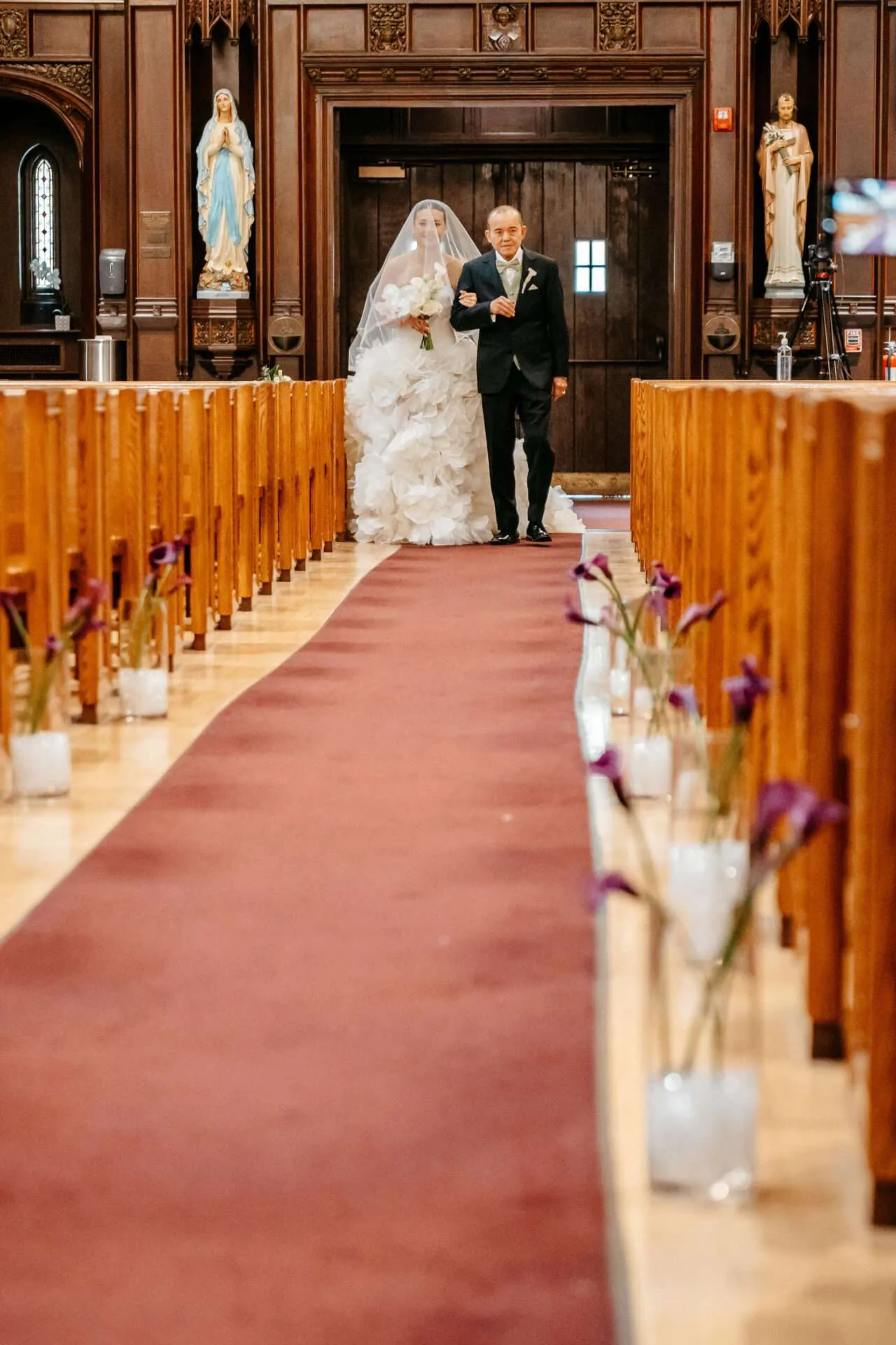 A bride walks down the aise with her father holding a white bouquet desiged by the best wedding florist in boston