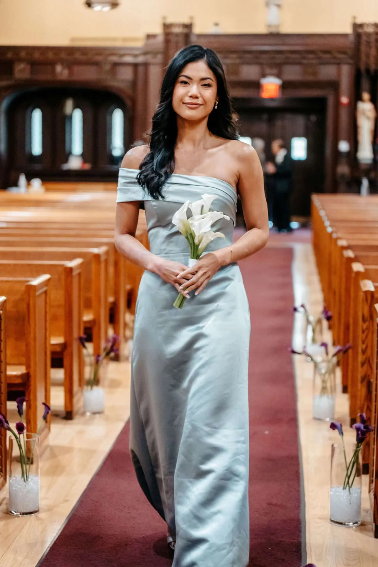 A bridesmaid in a teal dress walks down the aisle with a white bouquet arranged by a wedding florist in massachusetts
