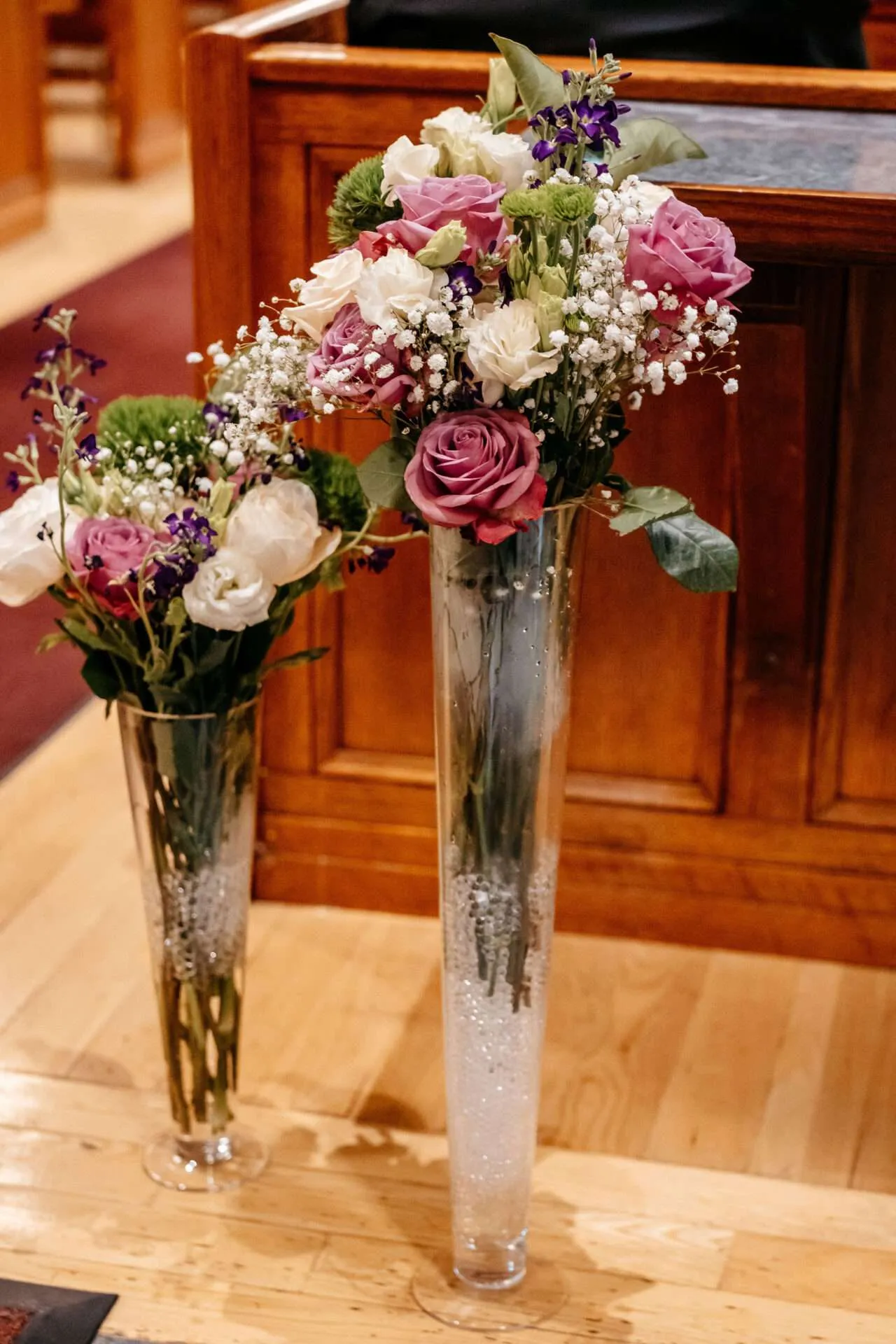 Two tall flower arrangements of pink, white, purple, and green by a wedding florist in Boston decorate a wedding reception area
