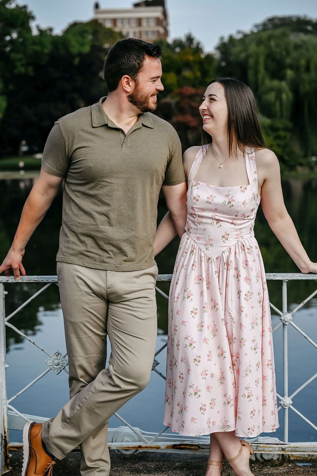 A couple smiles on a bridge in front of a river talking about restaurants in boston for date night