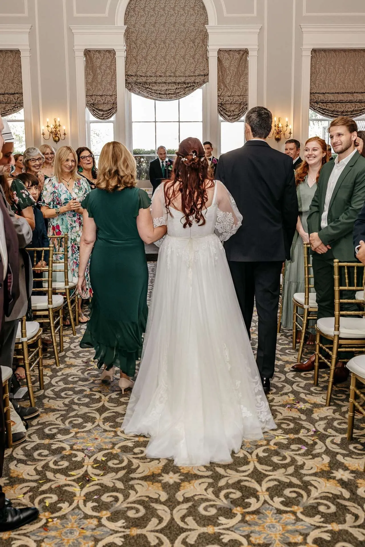 A bride walks down the aisle at her wedding ceremony with her mother and father at one of the hotel wedding venues in boston.
