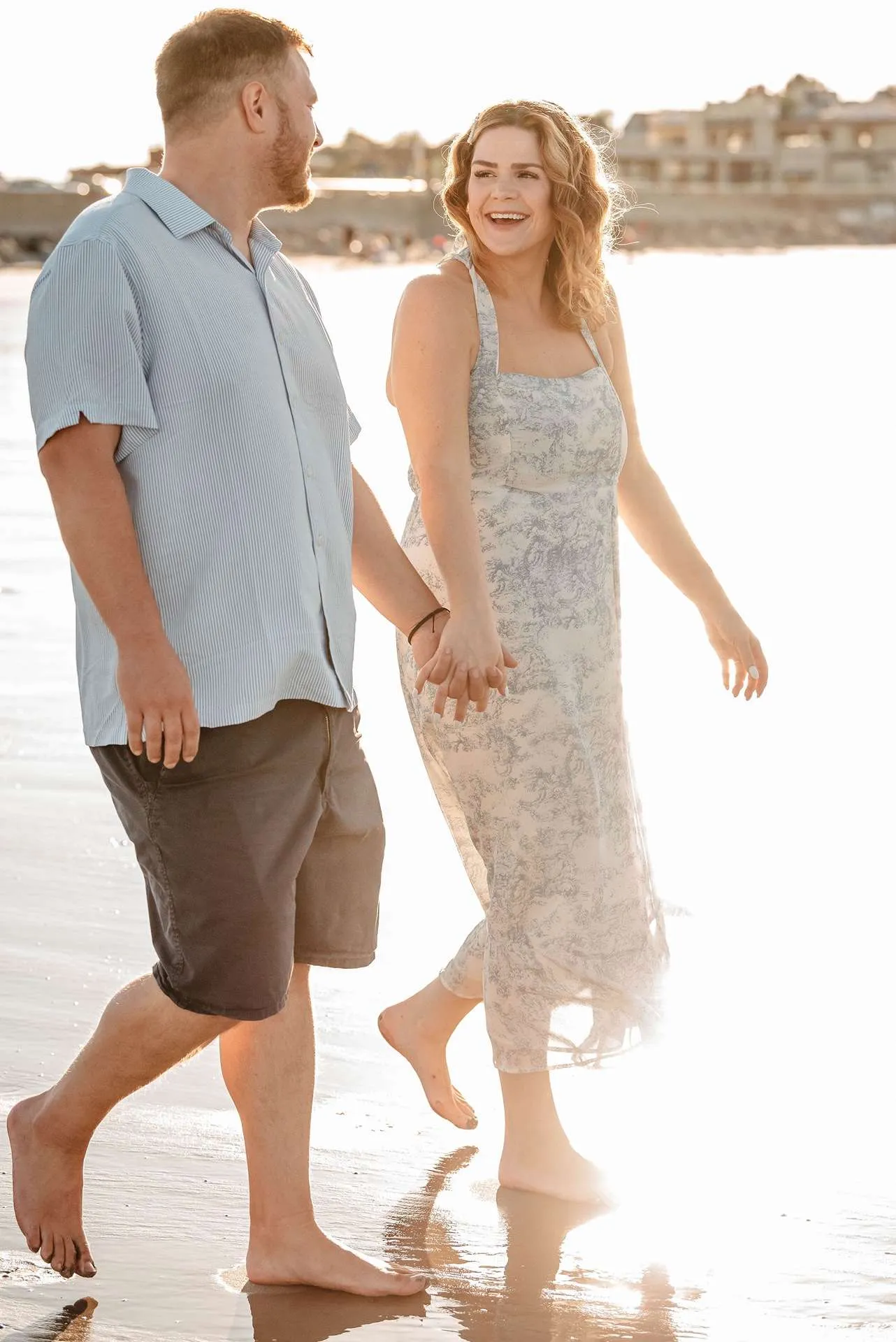 A couple smiles and laughs together while holding hands walking down the beach knowing fun date ideas in boston ma.