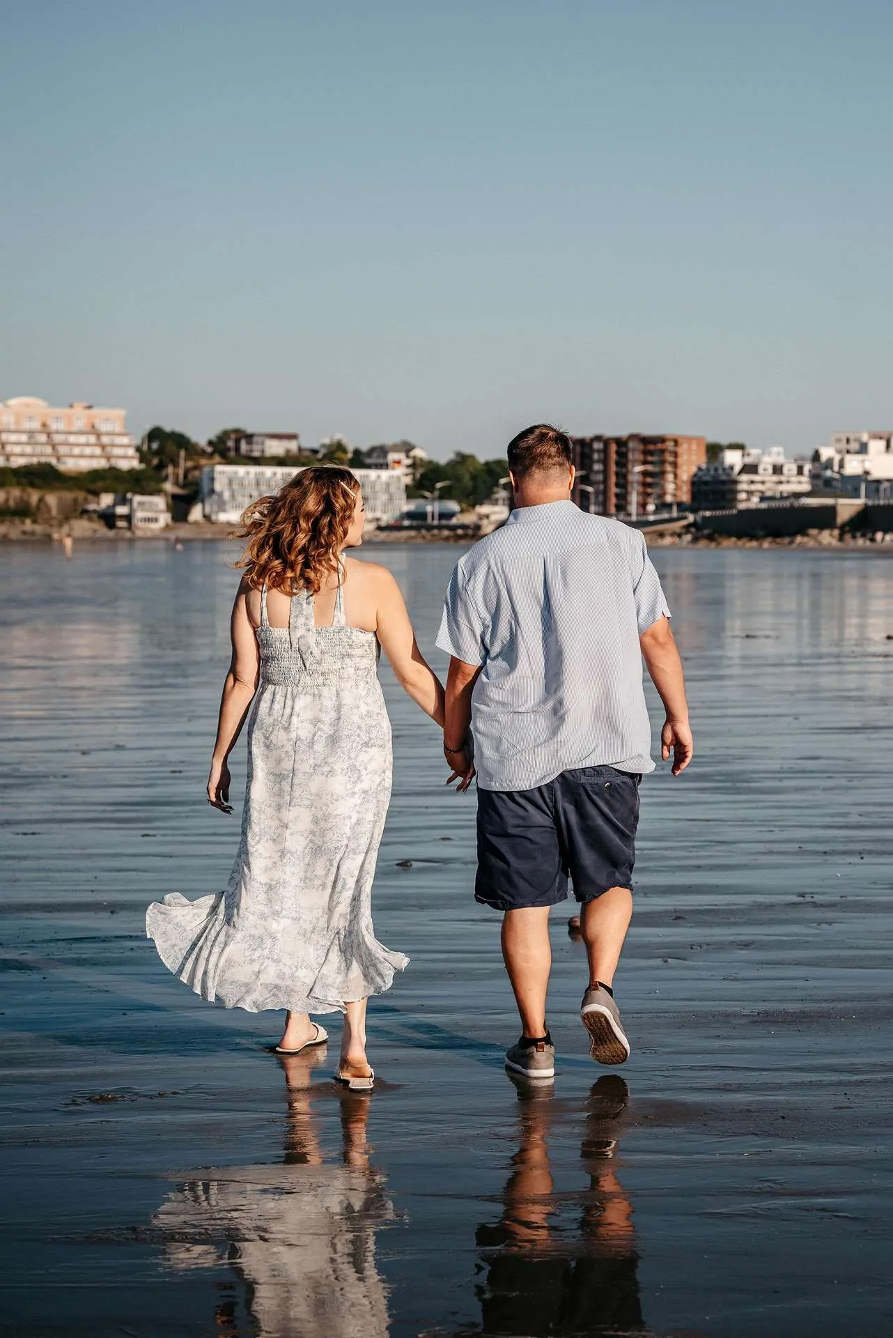 A couple walks down the beach holding hands and discussing fun date night ideas in boston.