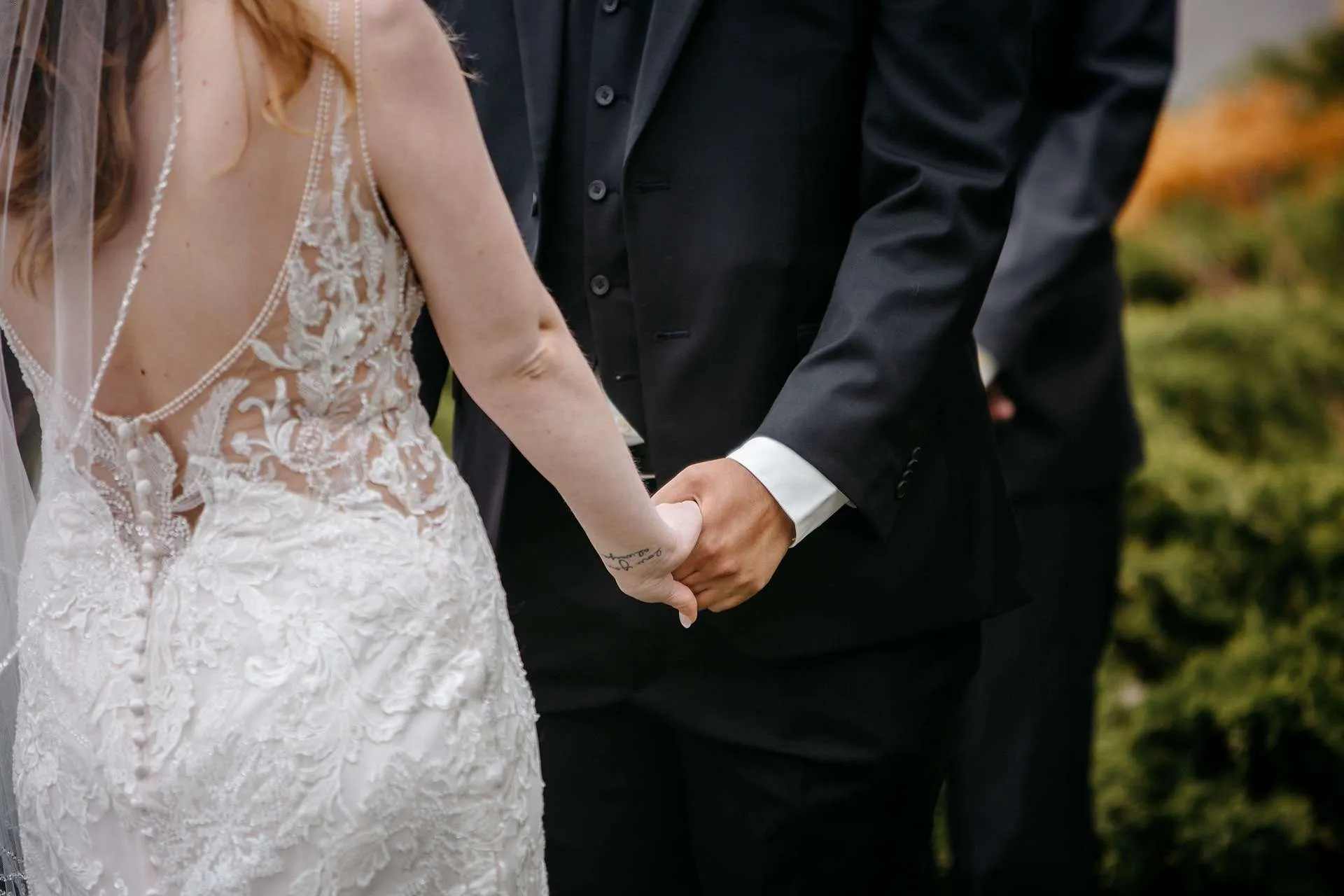 A photographer in boston takes a photo of a bride in a lace wedding dress holding hands with her groom.