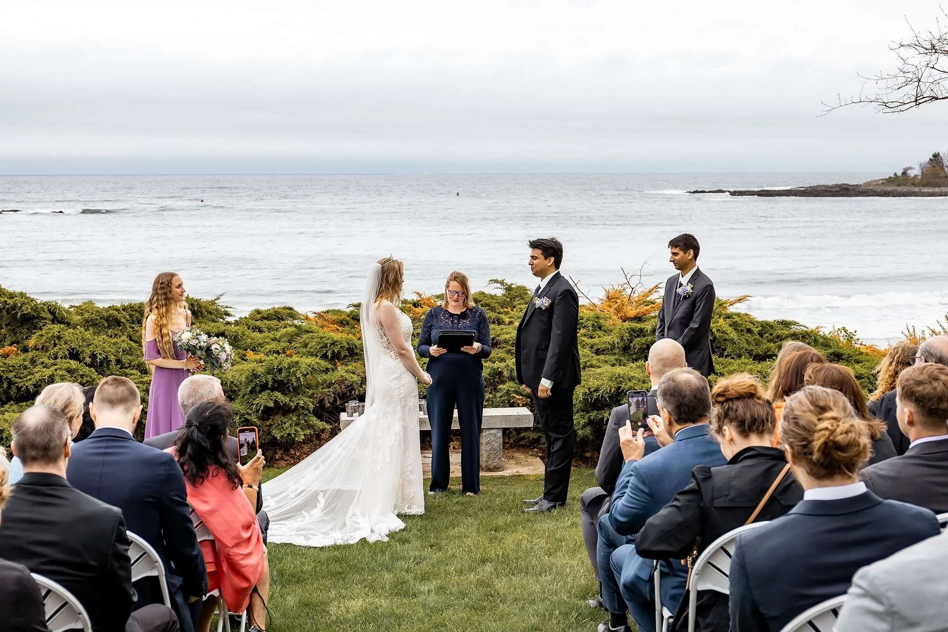 Photographers in boston capture priceless moments as a bride and groom say their vows on a coastal venue with the ocean in the background.