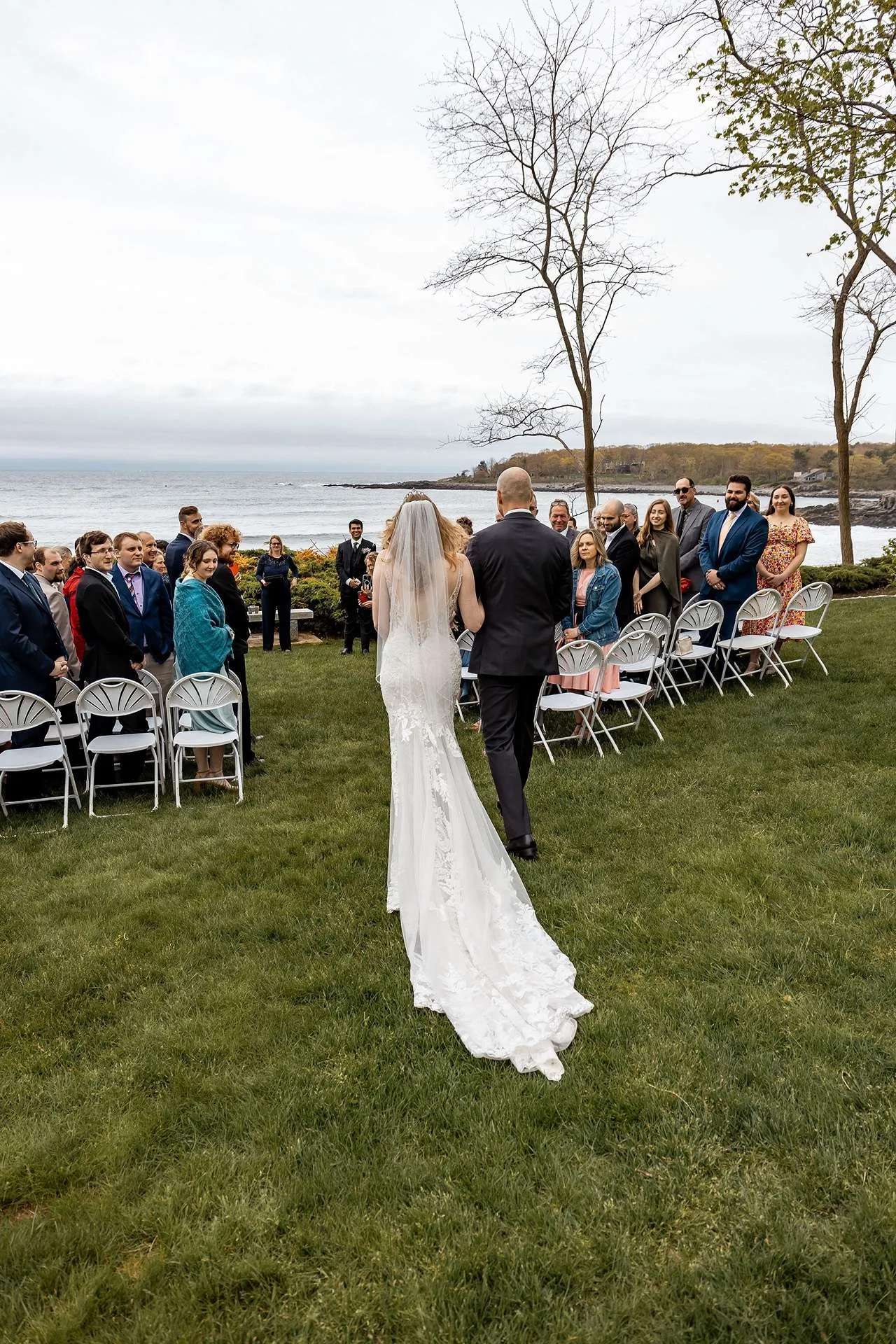 A photographer in boston stands behind a bride and her father taking photos as they walk down the aisle.