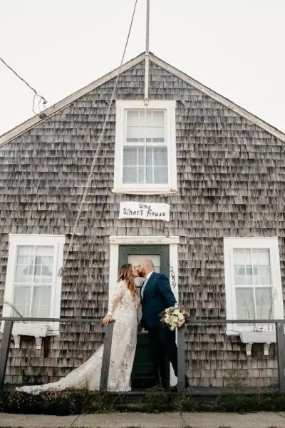 A bride and groom kiss on the porch of the iconic Wharf House during their wedding in Provincetown, Cape Cod, Massachusetts.